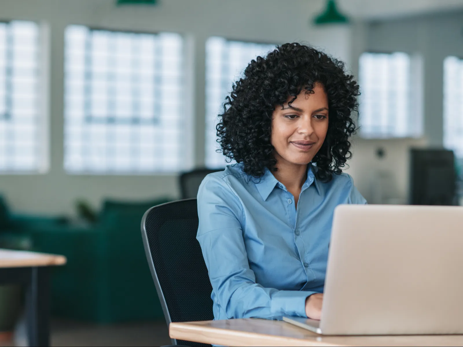 Woman with curly hair working on a laptop in a modern office environment.