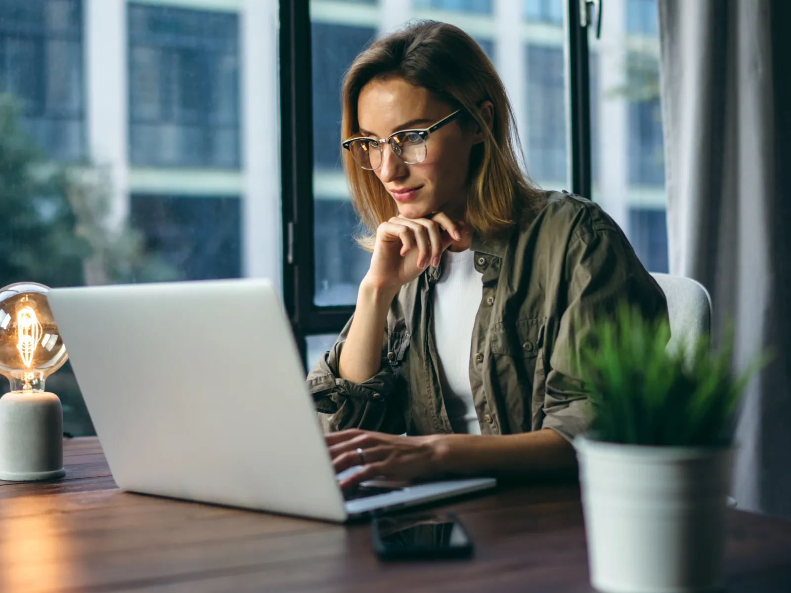 Young woman working on a laptop at a stylish home workspace with natural light.
