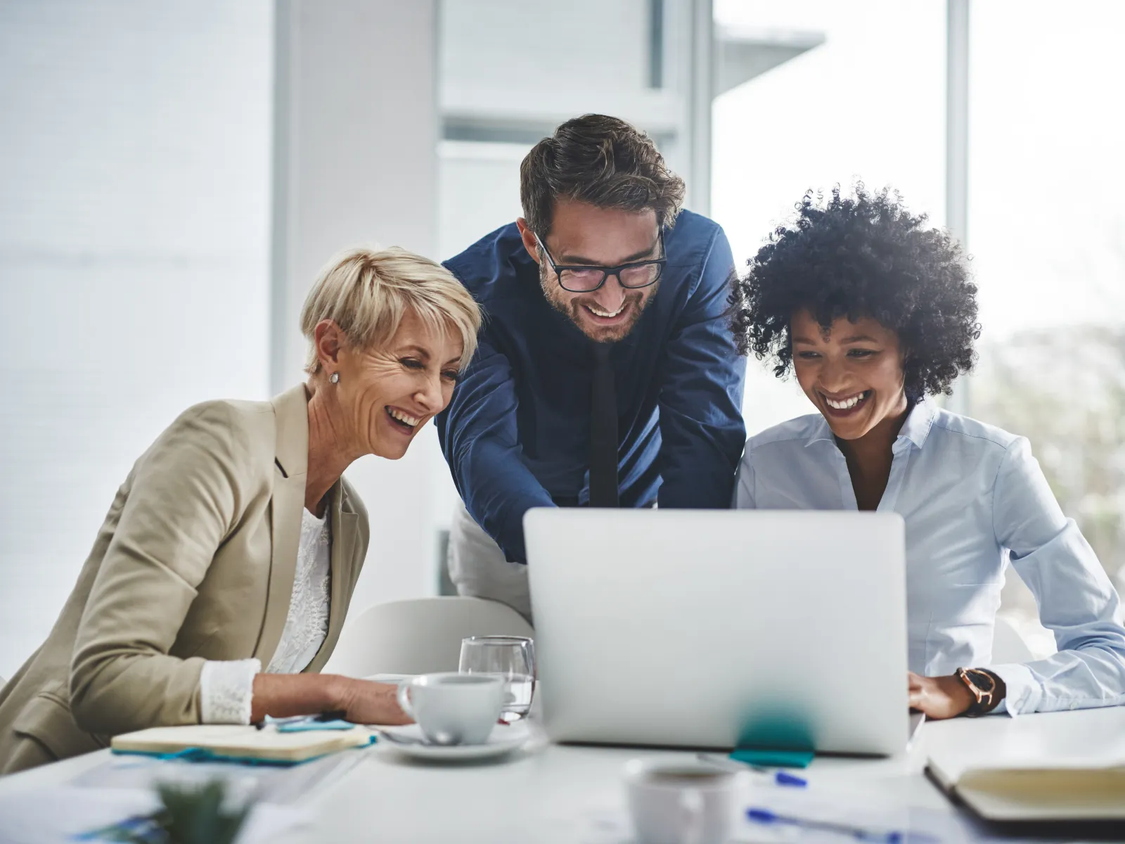 Three professionals collaborating over a laptop in a modern office setting, smiling and engaged.
