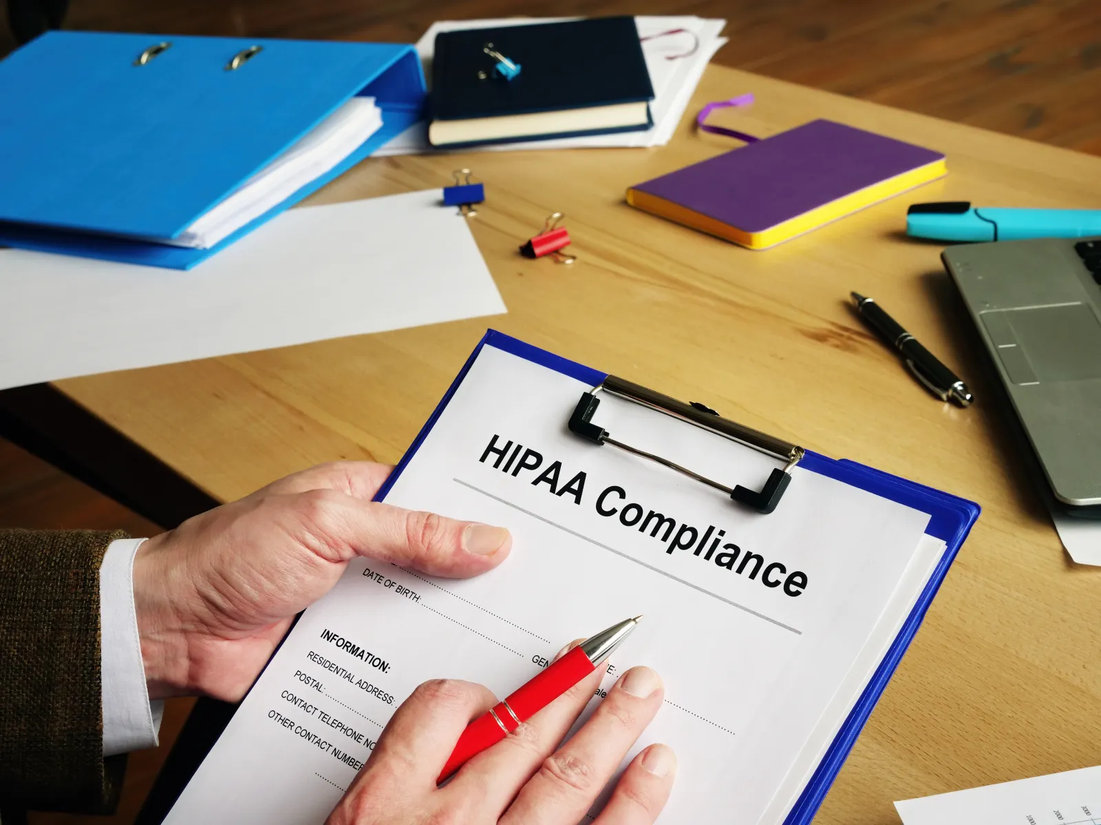 Person reviewing HIPAA compliance documents on a wooden desk with stationery and laptop in background.