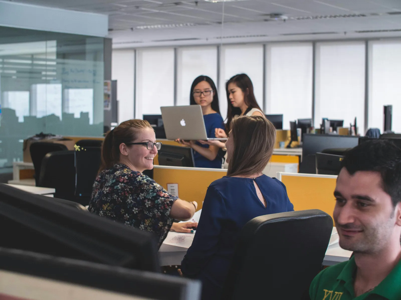 Team collaborating in an office with laptops and desks, showcasing a productive workspace atmosphere.
