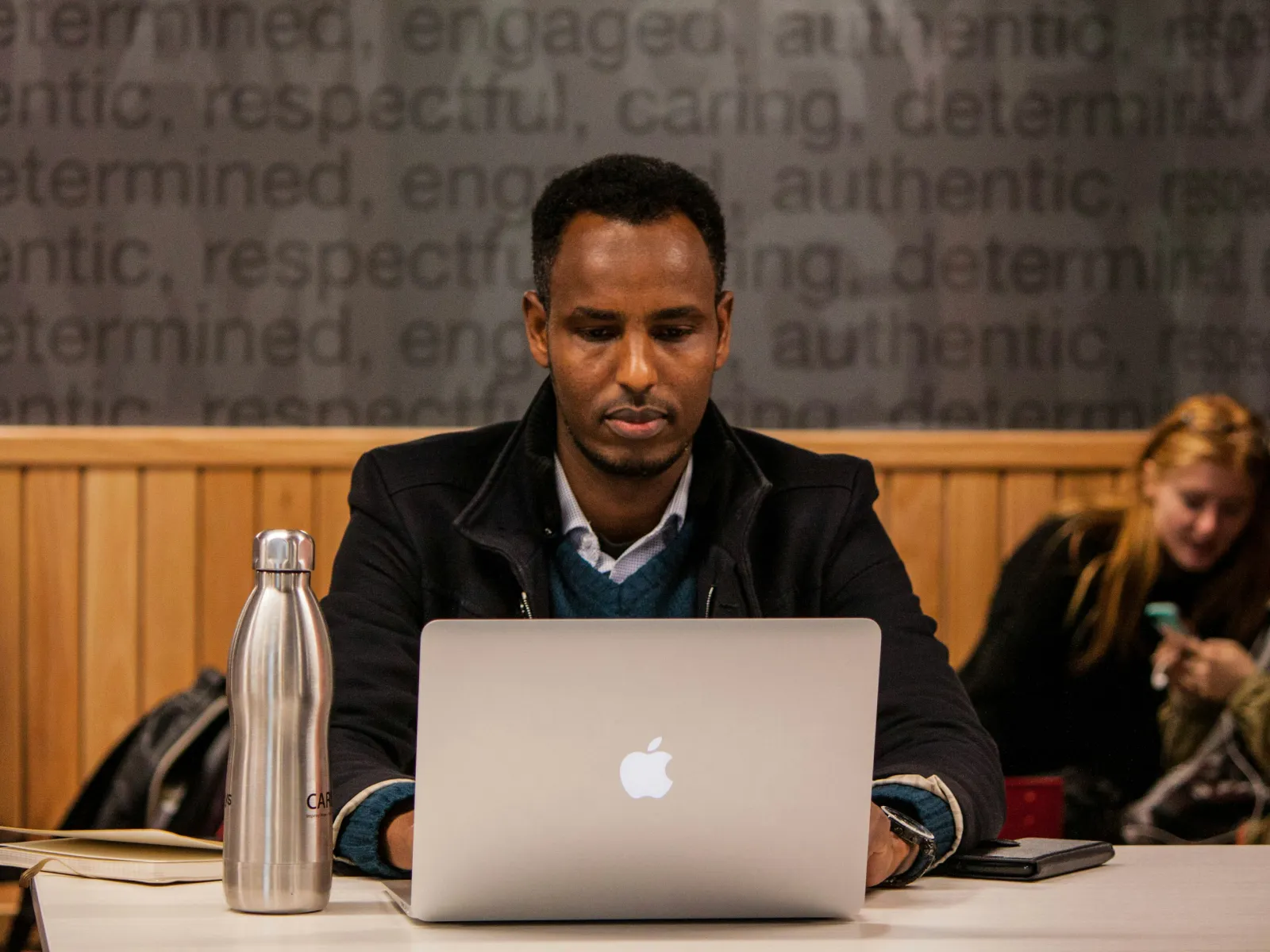 Focused man working on laptop in a casual coffee shop setting with other people in the background.