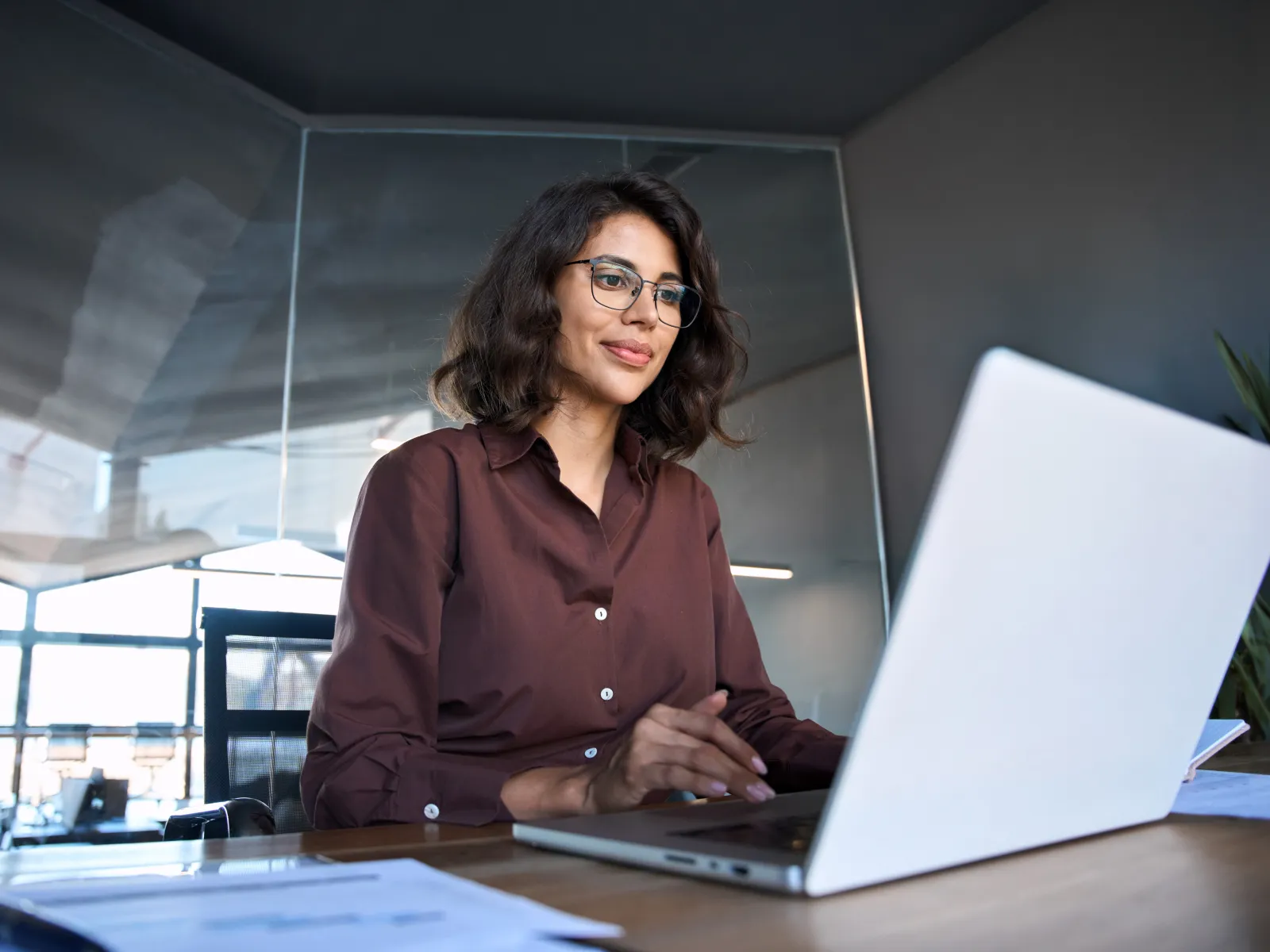 Smiling woman working on a laptop in a modern office setting with a bright atmosphere.