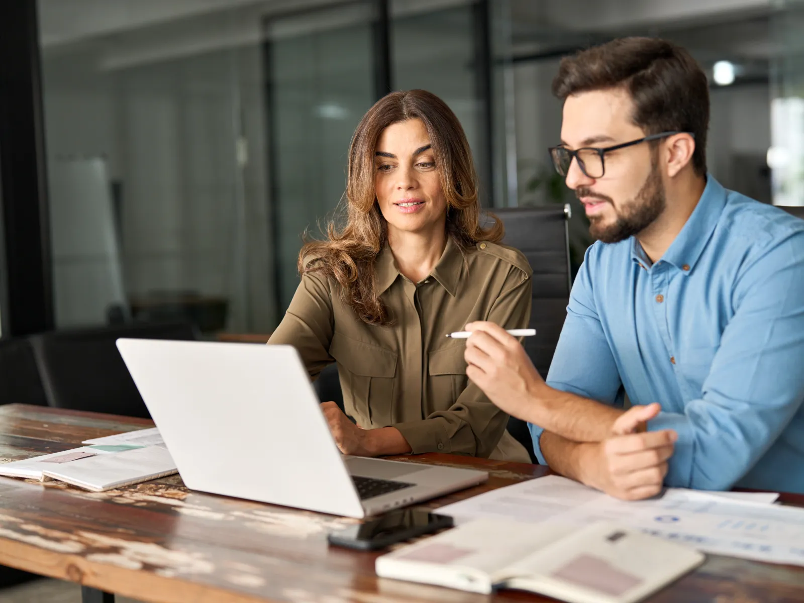 Two professionals collaborating over a laptop in a modern office setting.