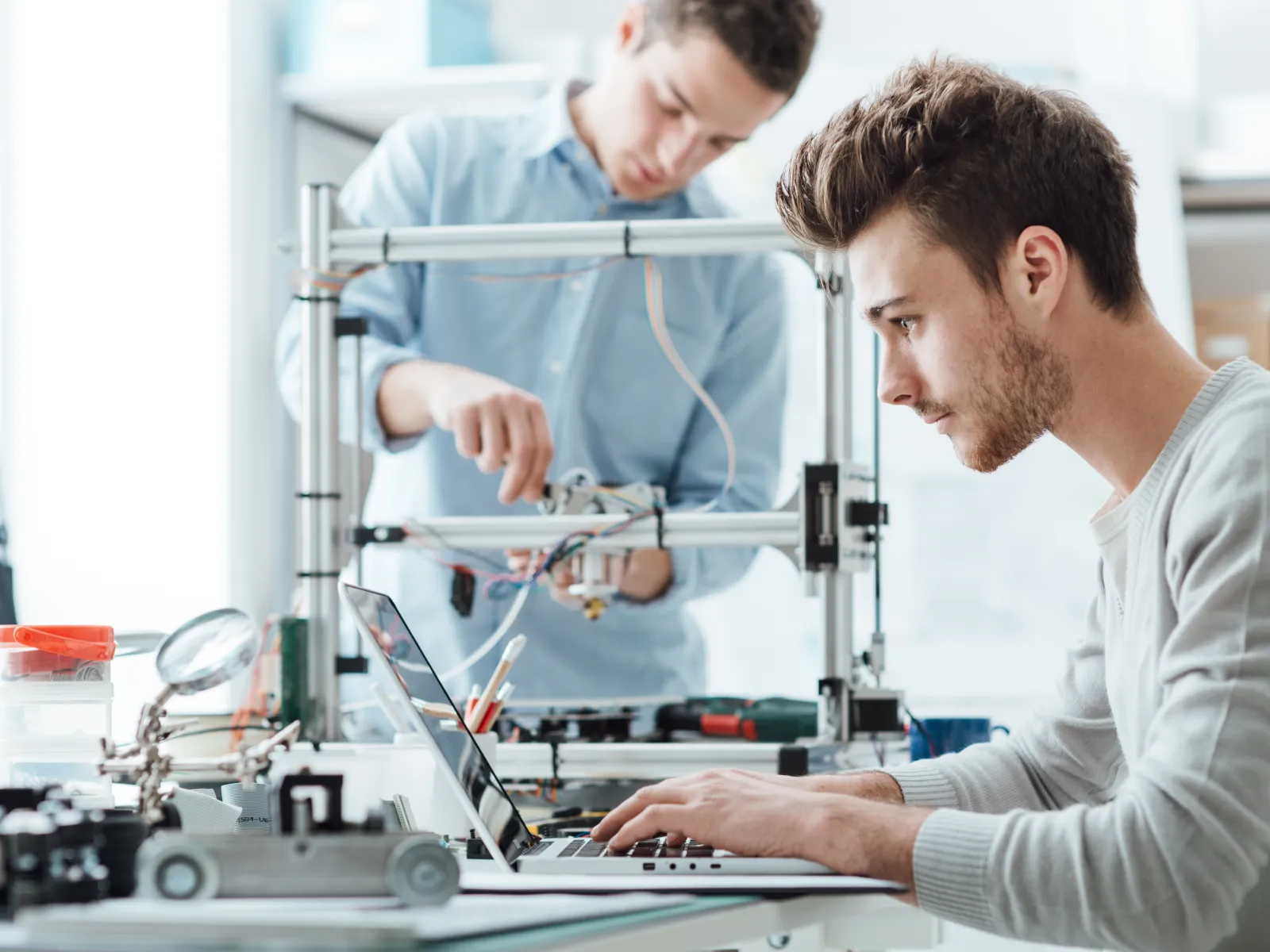 Two engineers working on robotic projects with tools and laptop in a modern workspace.