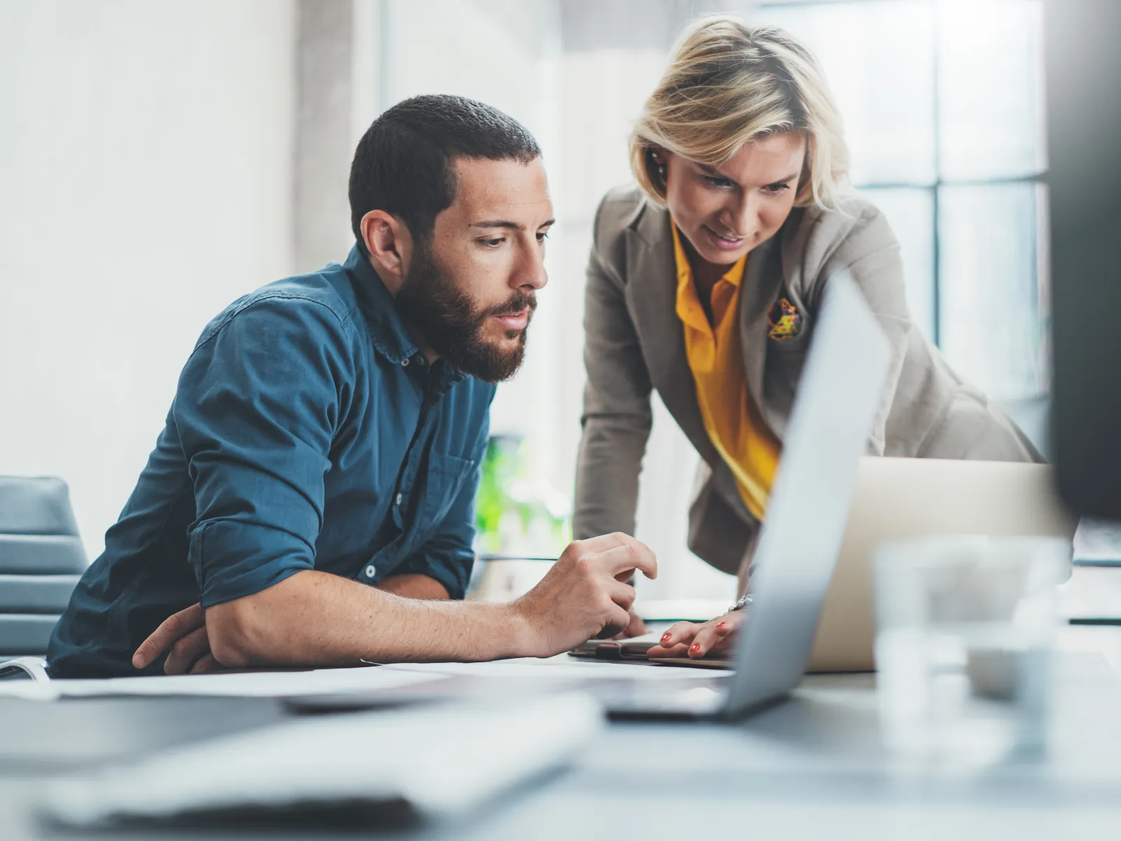Two professionals collaborating over a laptop in a modern office setting.
