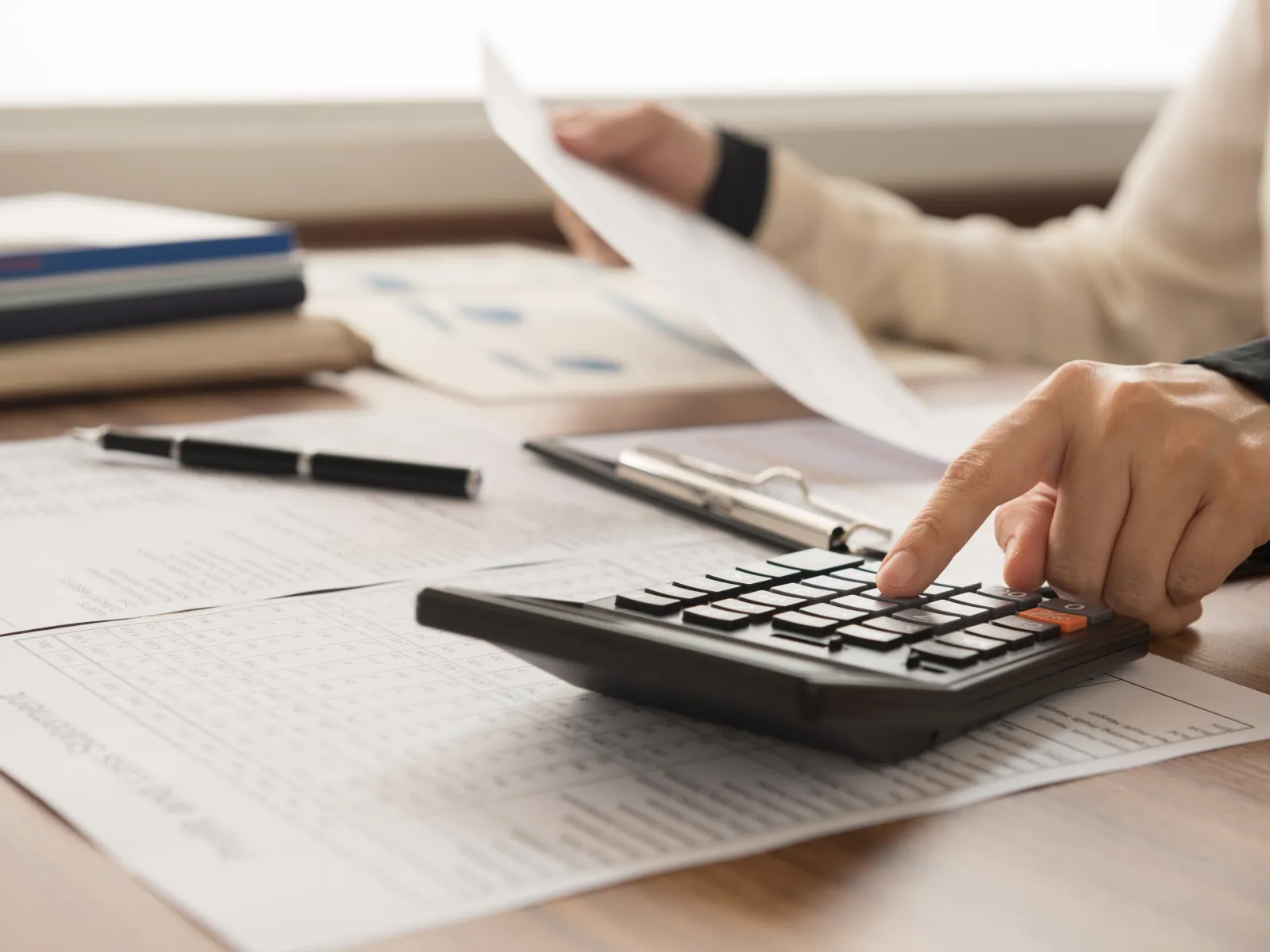 Close-up of a person using a calculator on a desk with financial documents and stationery.