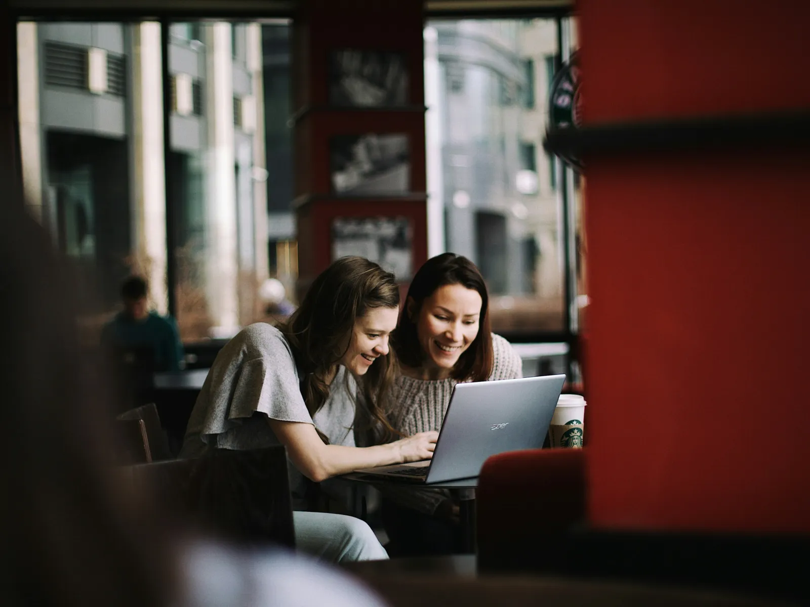 Two women collaborating on a laptop in a cozy coffee shop setting.