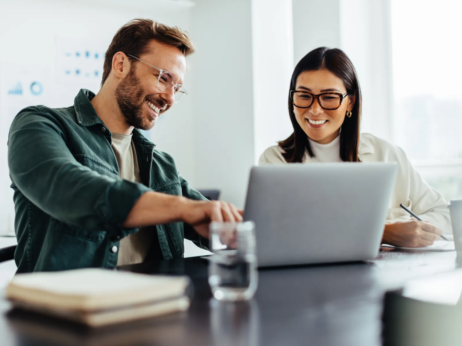 Two colleagues collaborating on a laptop in a modern office setting, smiling and engaged.