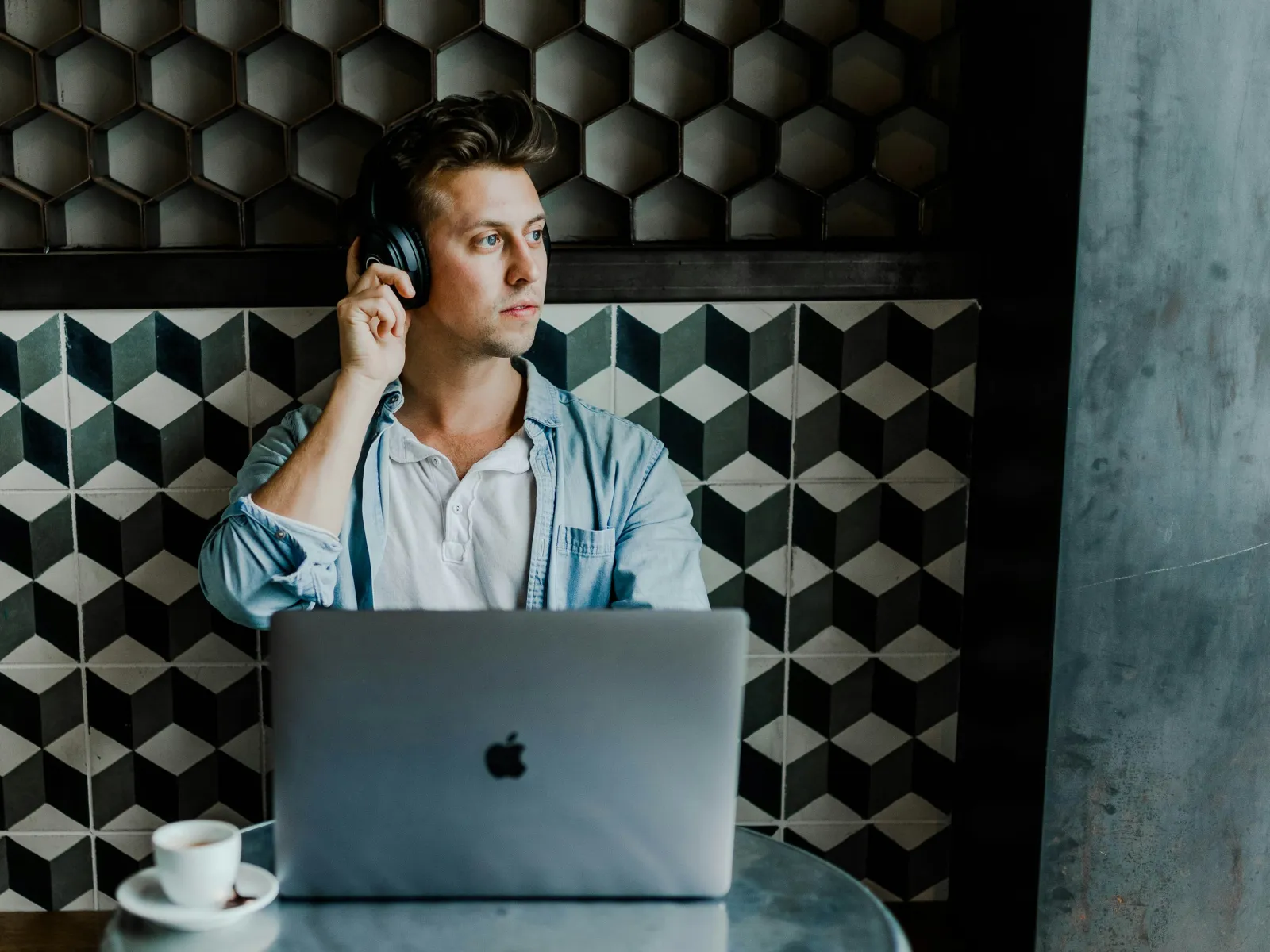 A young man uses headphones while working on a laptop in a stylish cafe with geometric decor.