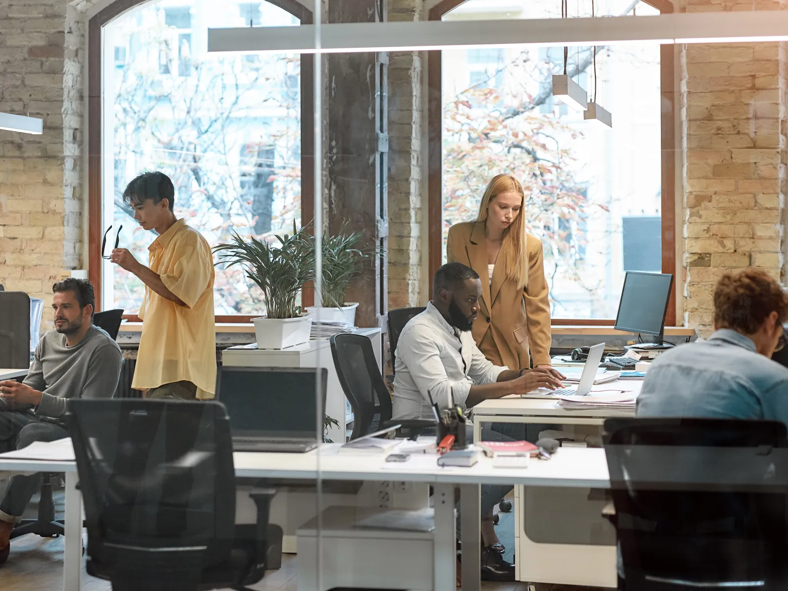 Modern office space with diverse people collaborating at desks and discussing ideas.