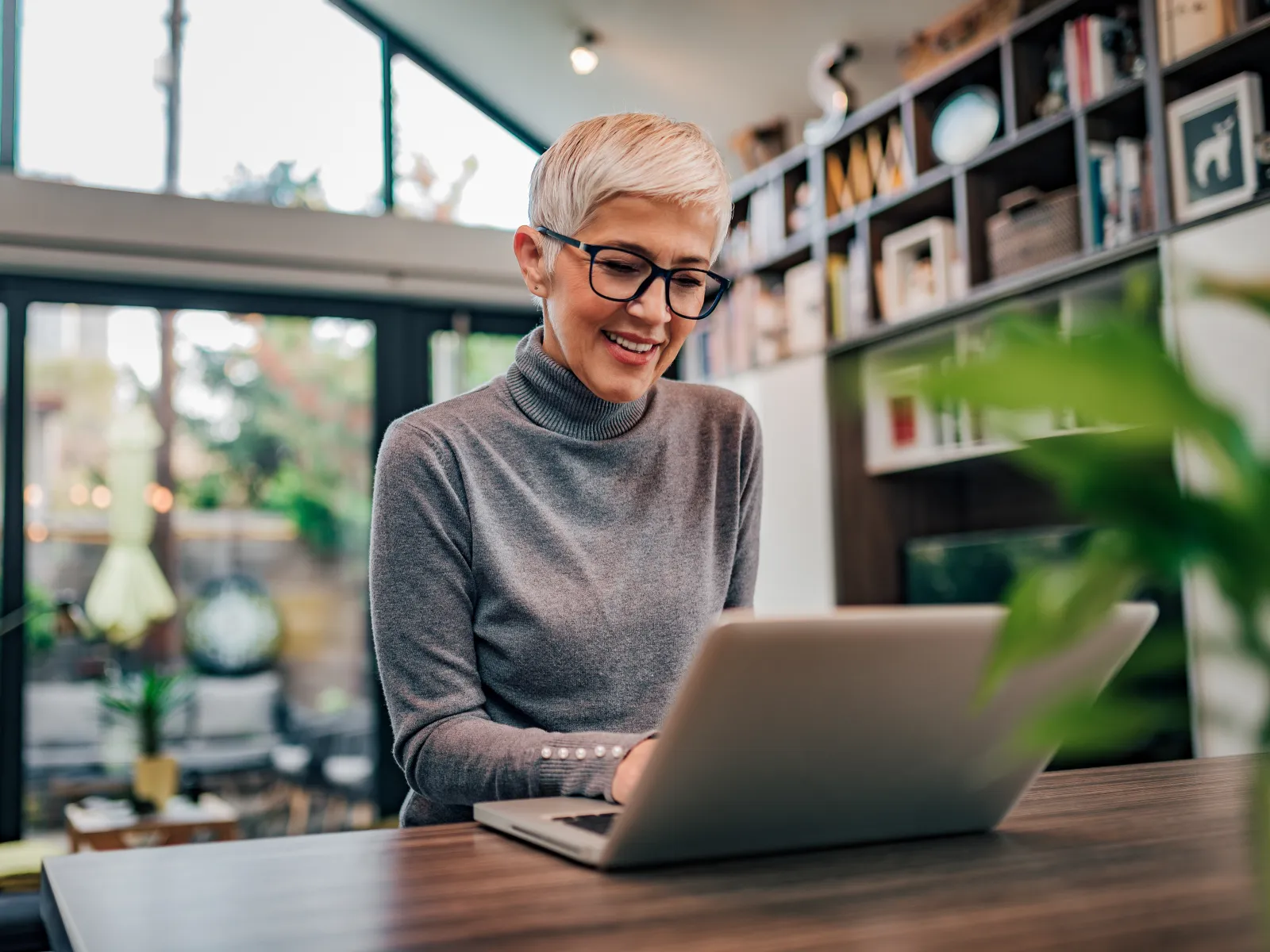 Smiling woman using a laptop at home in a bright, modern living space with plants.
