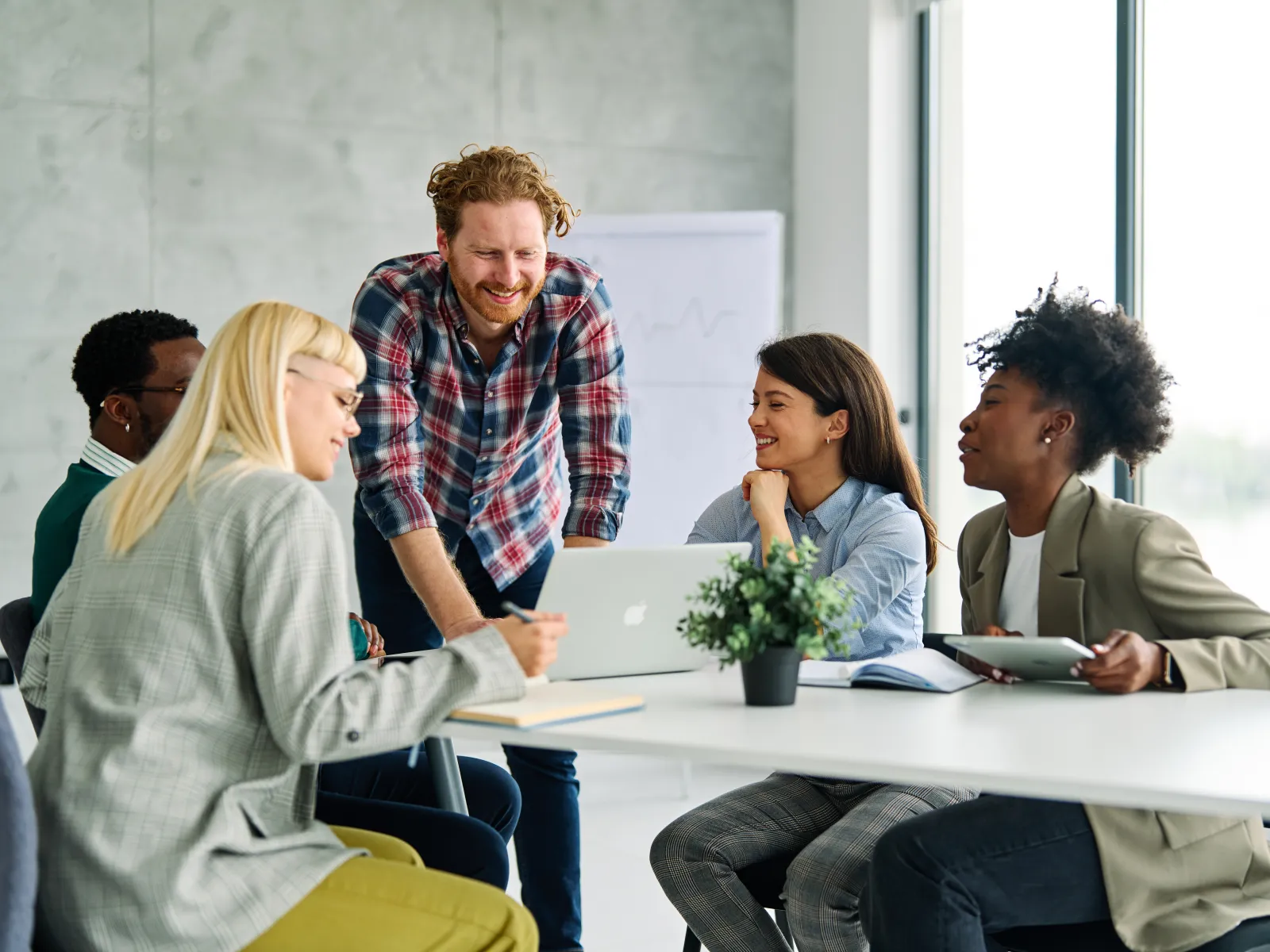 Diverse group of five colleagues collaborating around a table with laptop, notebook, and tablet in a modern office.