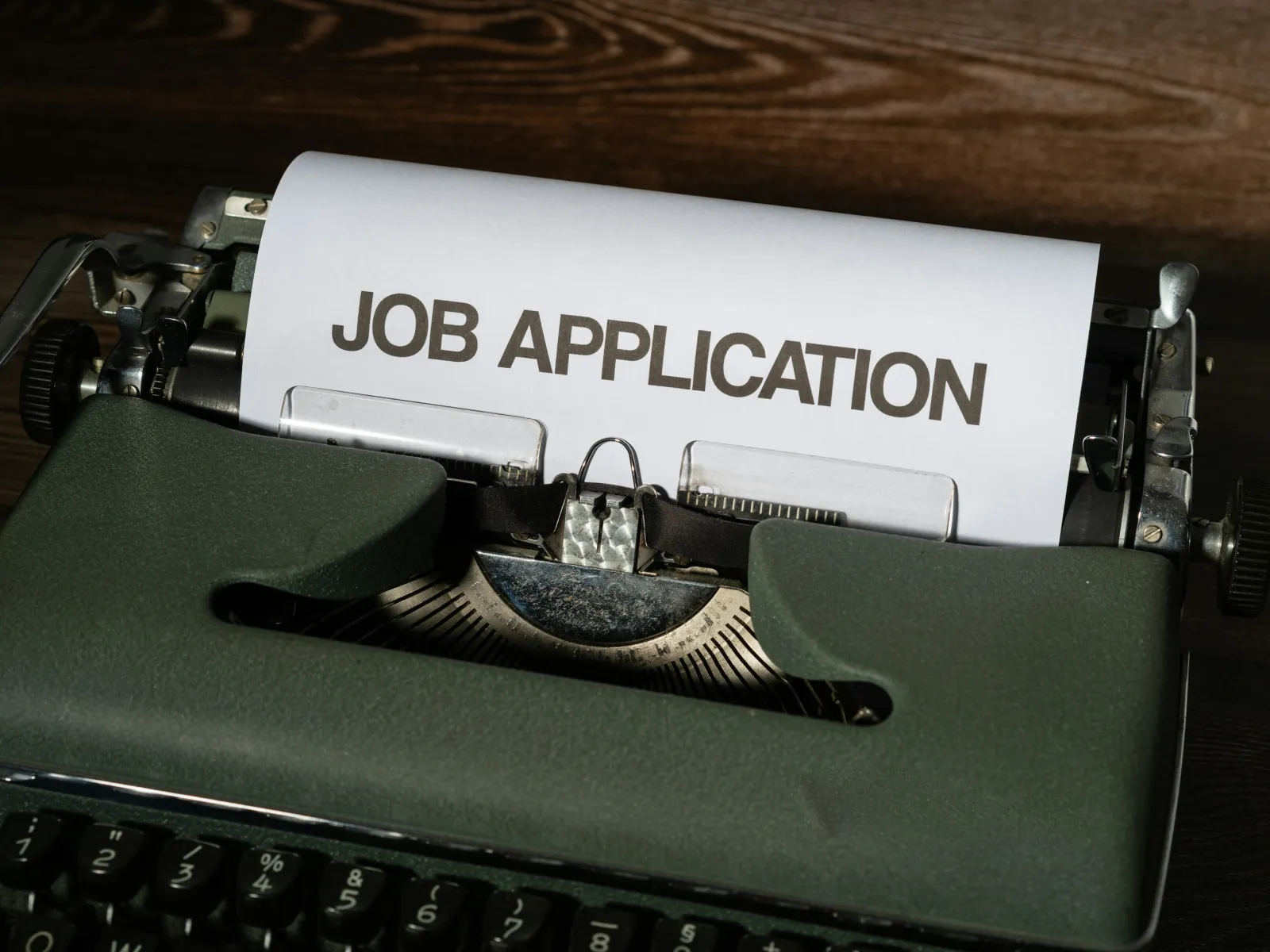 Close-up of a vintage typewriter with a paper displaying the words JOB APPLICATION on a wooden surface.