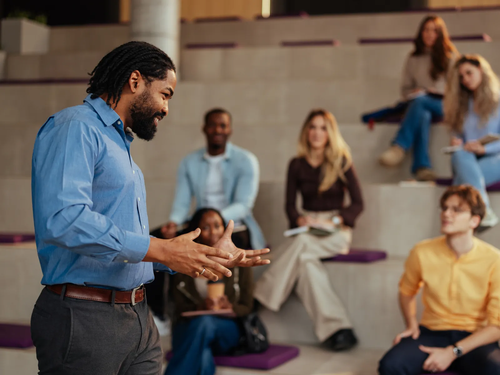 Man presenting to a diverse group of attentive students seated on tiered steps in a modern learning space
