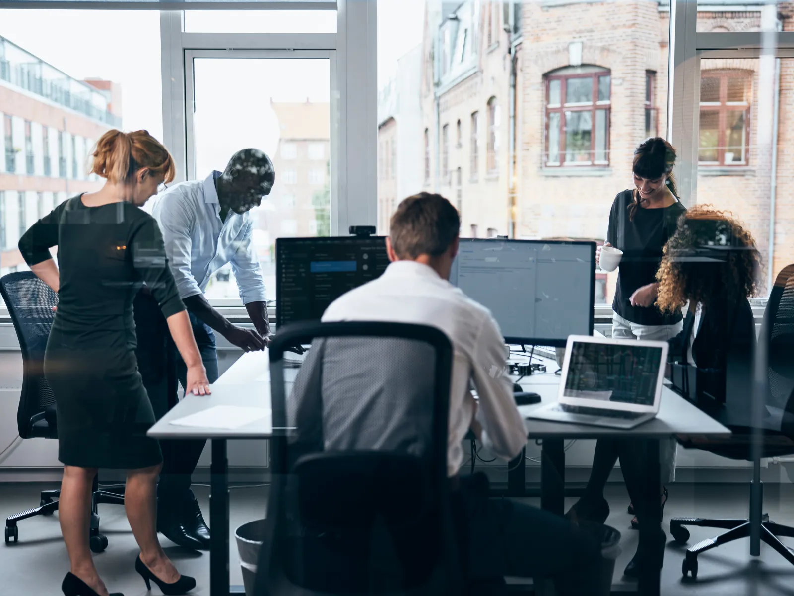 Group of professionals collaborating in a modern office setting with computers and charts visible.