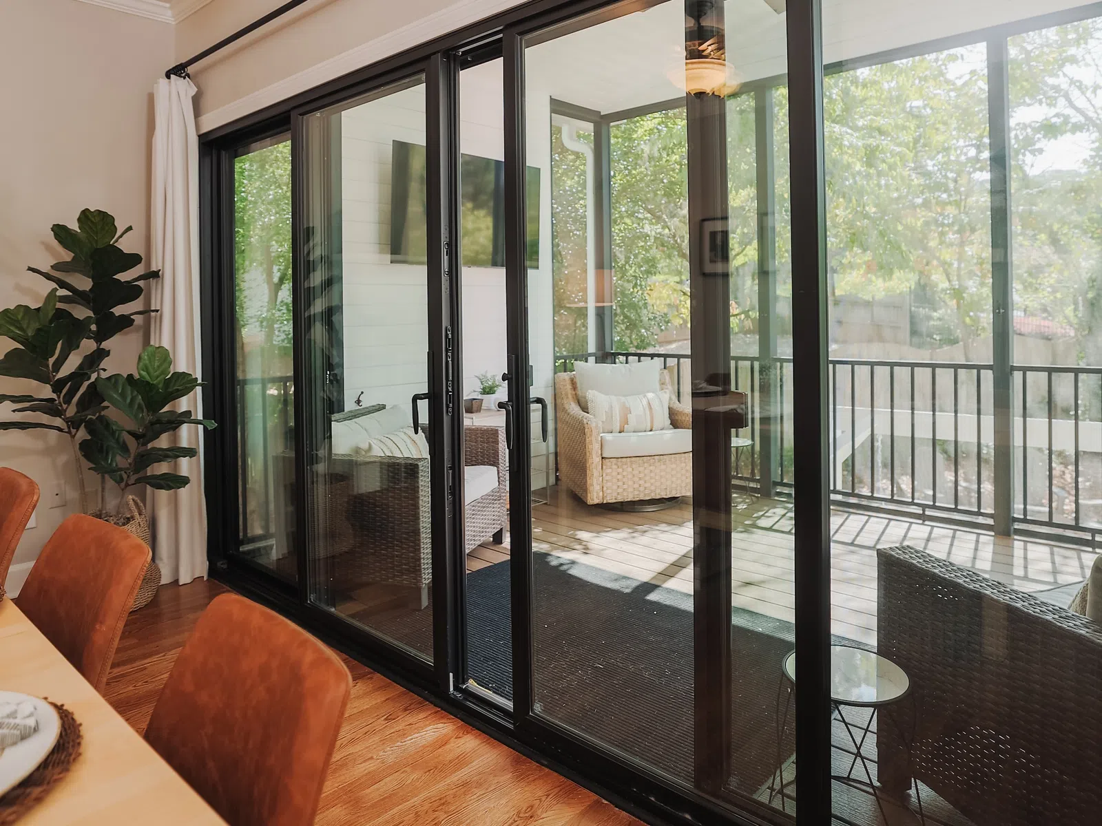 Spacious dining area with sliding glass doors leading to a cozy sunlit patio with wicker furniture and greenery.