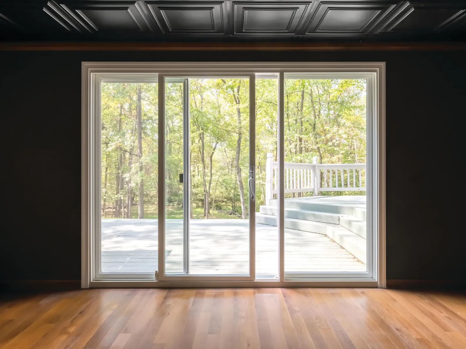Sliding glass door opening to a wooden deck and lush green forest outside on a sunny day