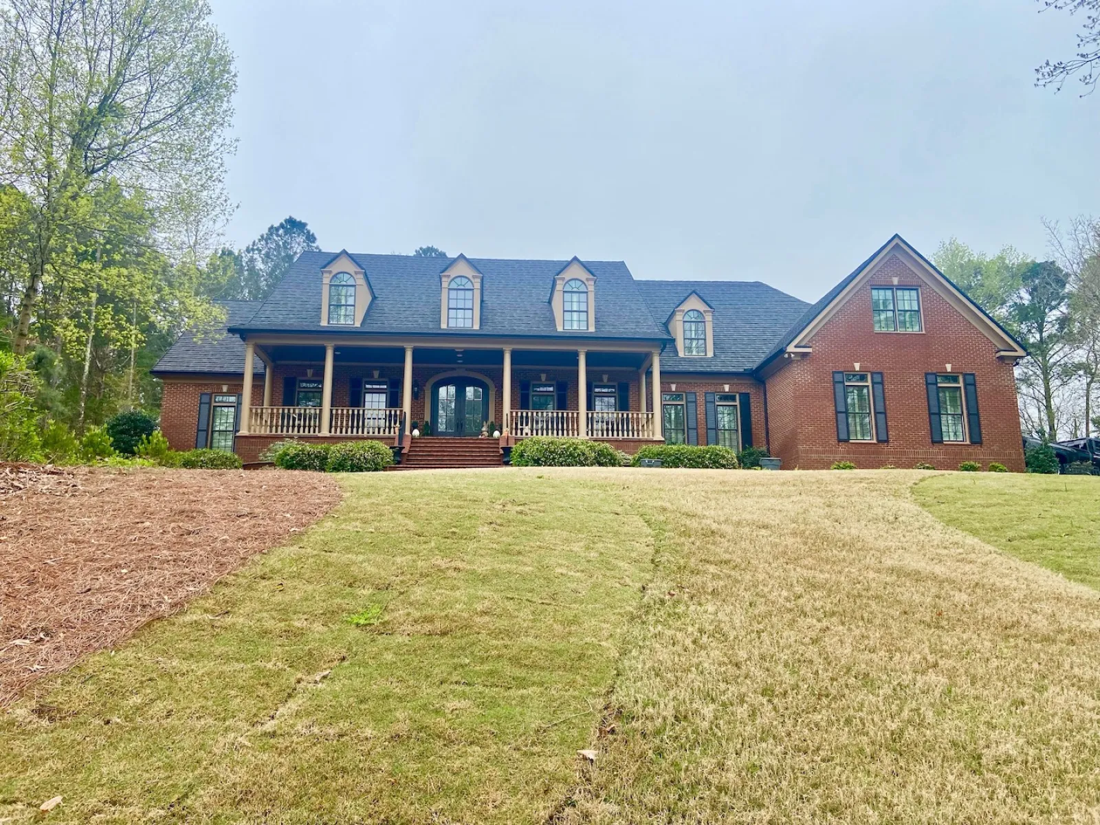 Large brick house with black shutters and a covered front porch on a spacious grassy lawn.