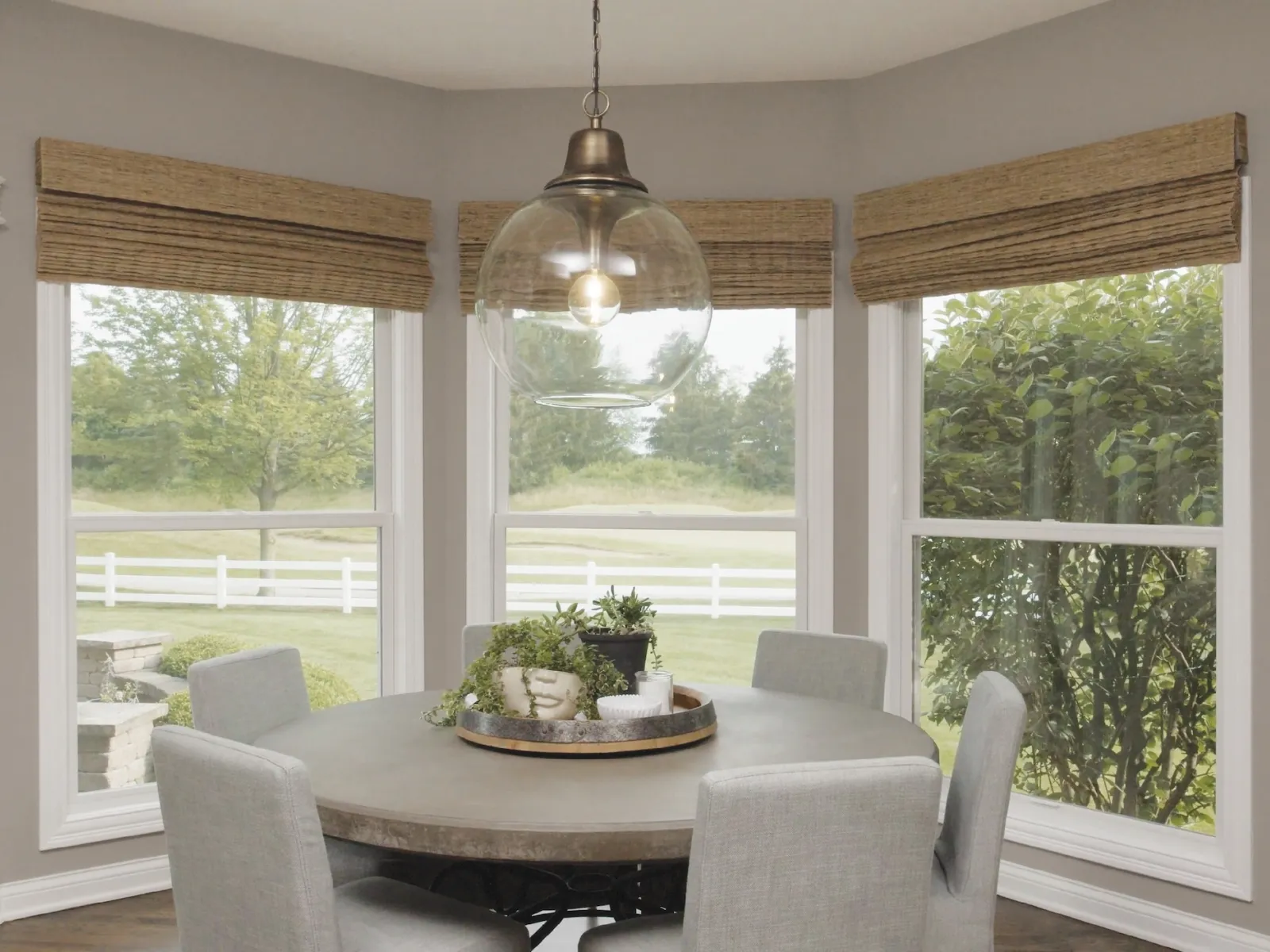 Cozy dining area with a round table, modern pendant light, and large windows showcasing green scenery.