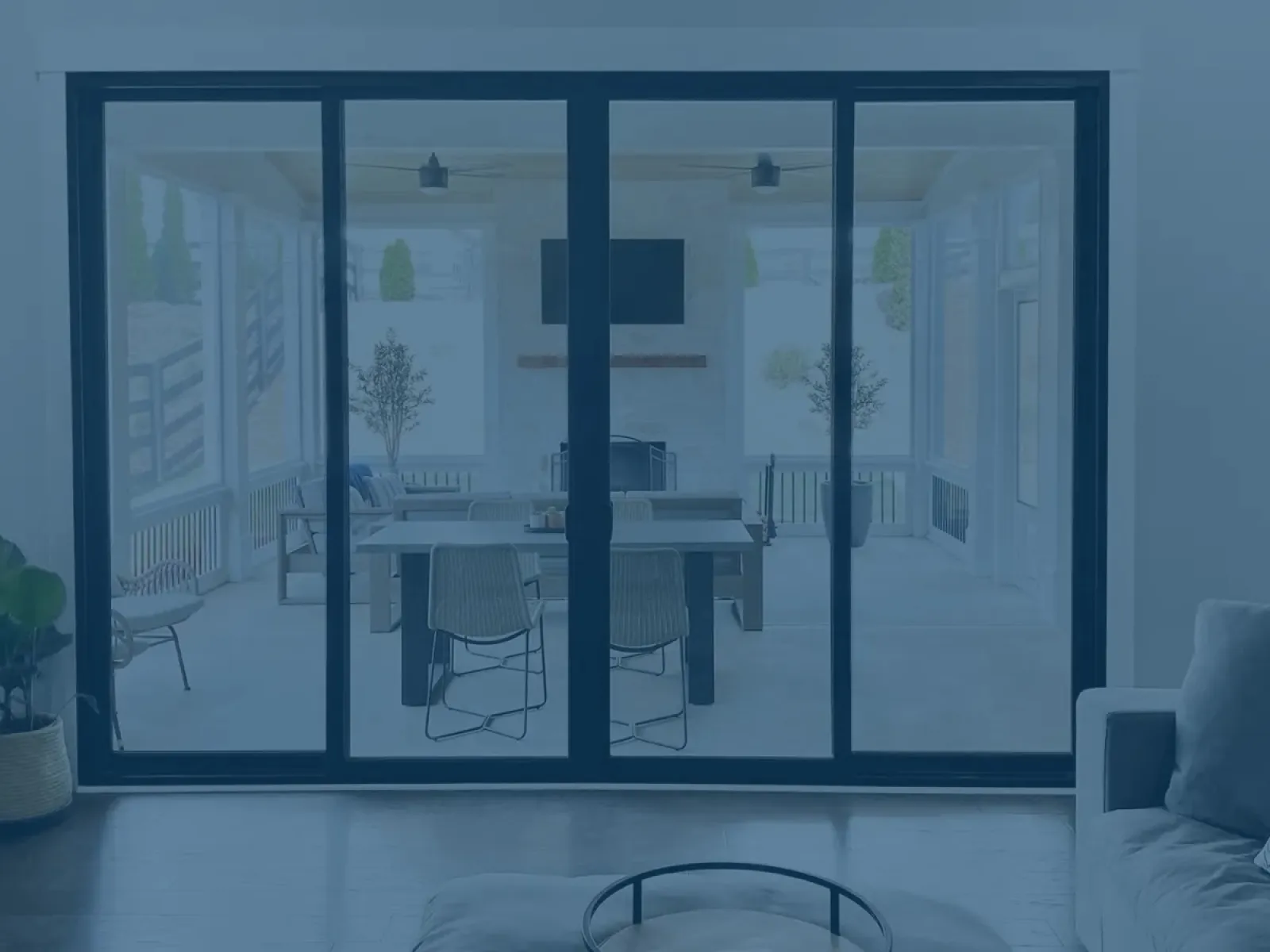Modern living room with gray sofa and sliding glass doors opening to a bright patio dining area with table and chairs.
