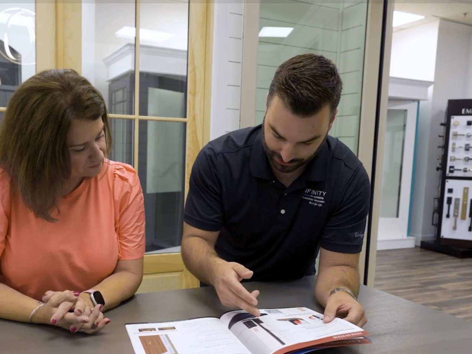 Man showing woman product catalog in a home improvement store with doors and hardware displays in background