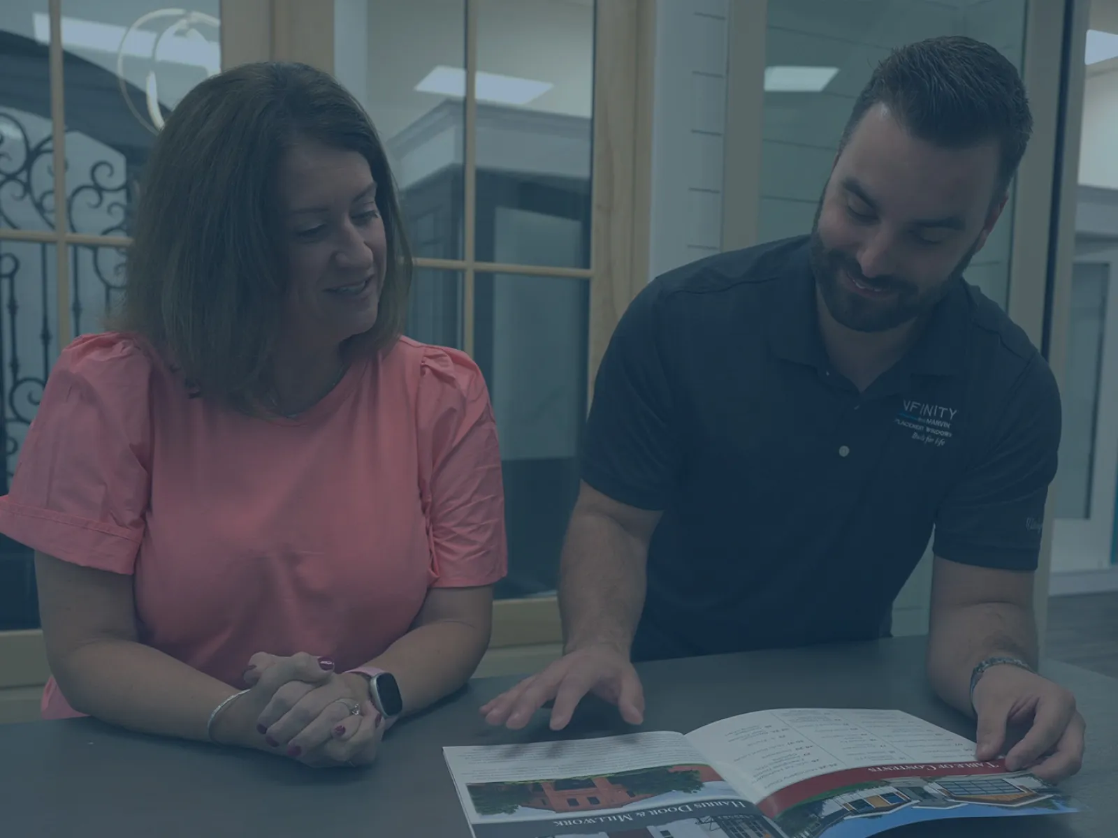 Man and woman discussing a brochure inside a modern office setting with glass windows and displays.