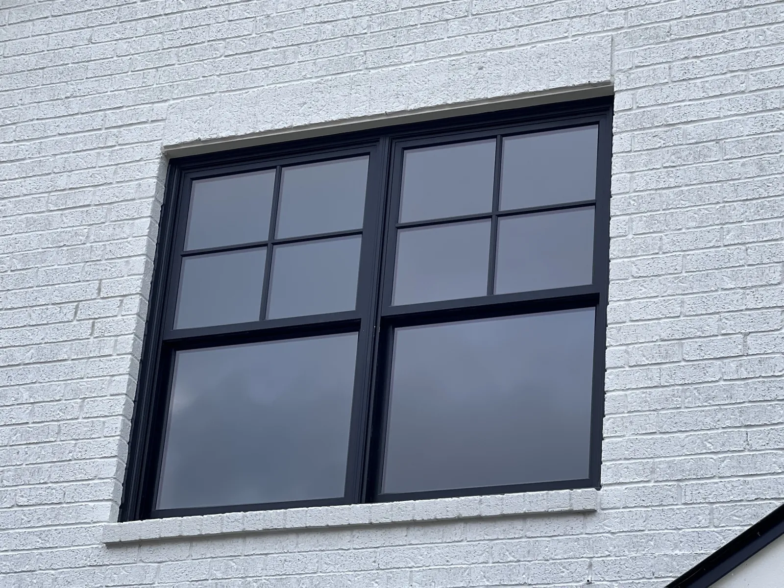 Modern black-framed window on white brick wall reflecting cloudy sky outdoors