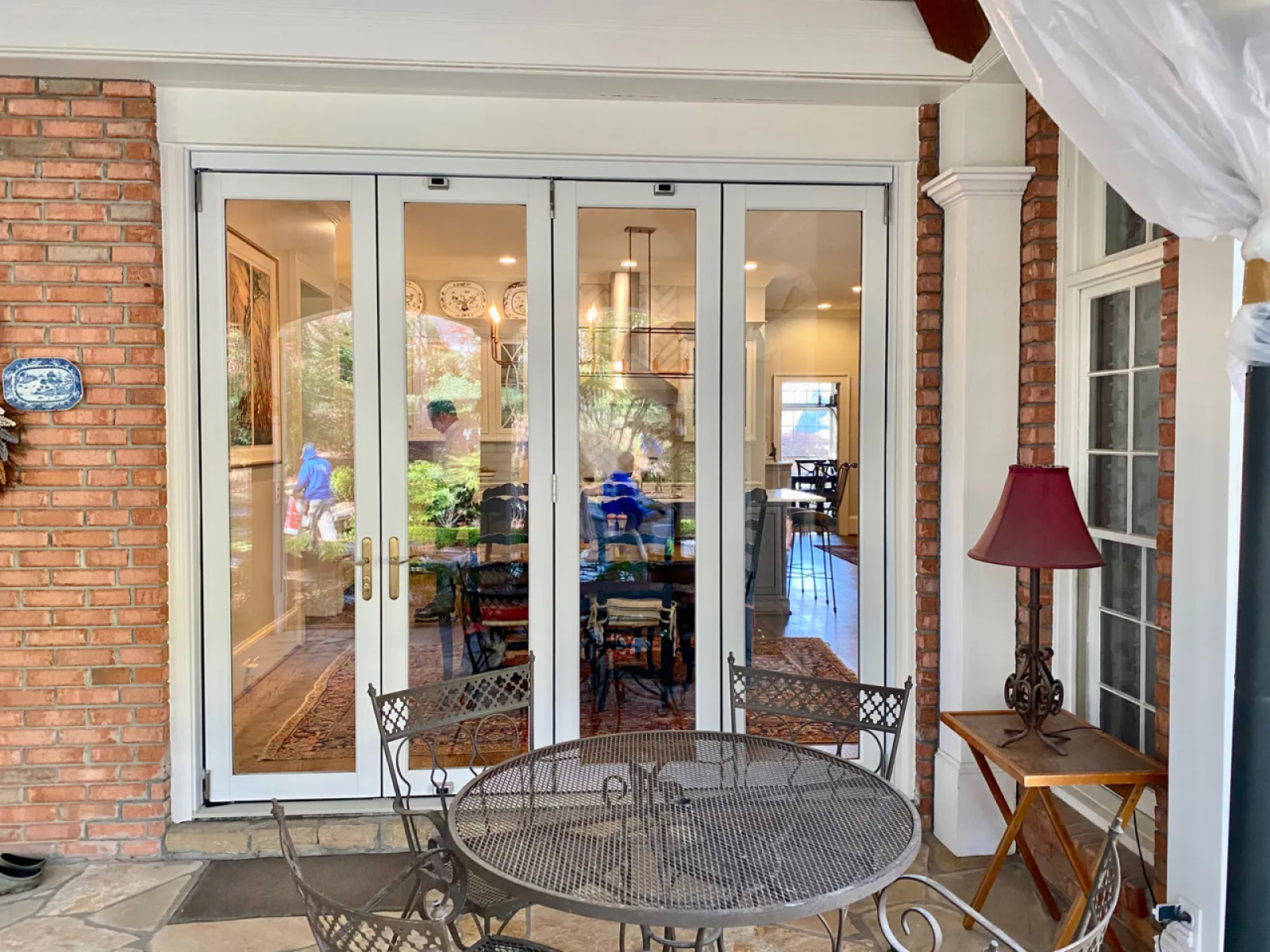 Outdoor patio with metal table and chairs in front of glass doors showing indoor dining area with people.