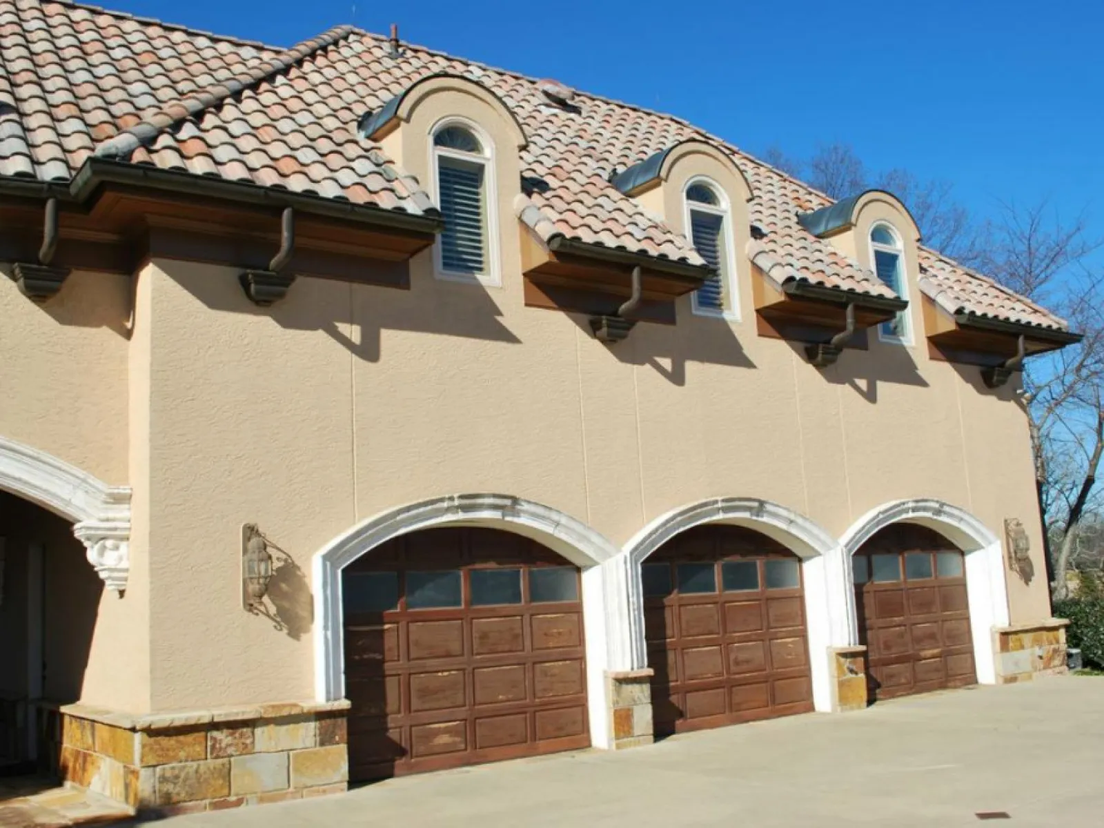 Mediterranean style house with three wooden garage doors and arched windows under tiled roof