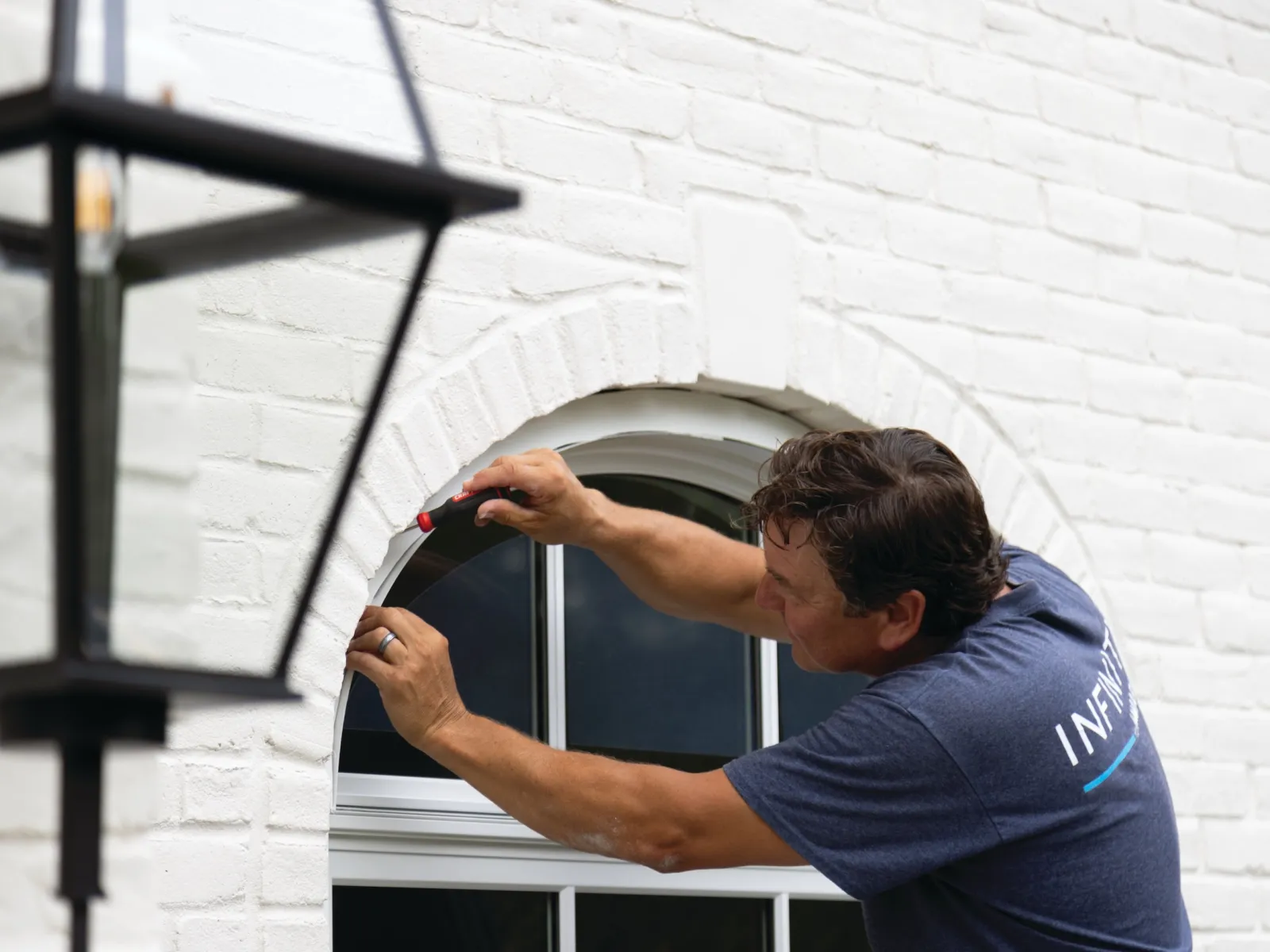 Worker installing or repairing window trim on a white brick house exterior during daytime.