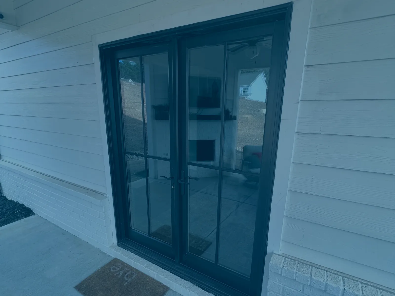 Black framed glass double doors leading to an outdoor patio with white siding and a concrete floor.