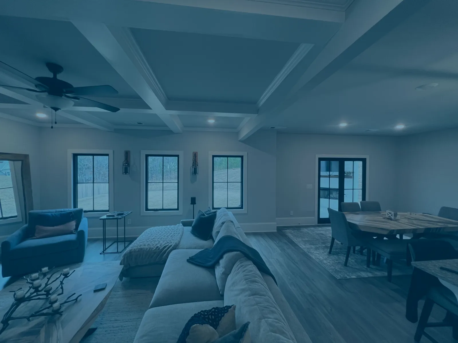 Spacious living room with gray sectional sofa, blue armchair, wooden dining table, and coffered ceiling with fan