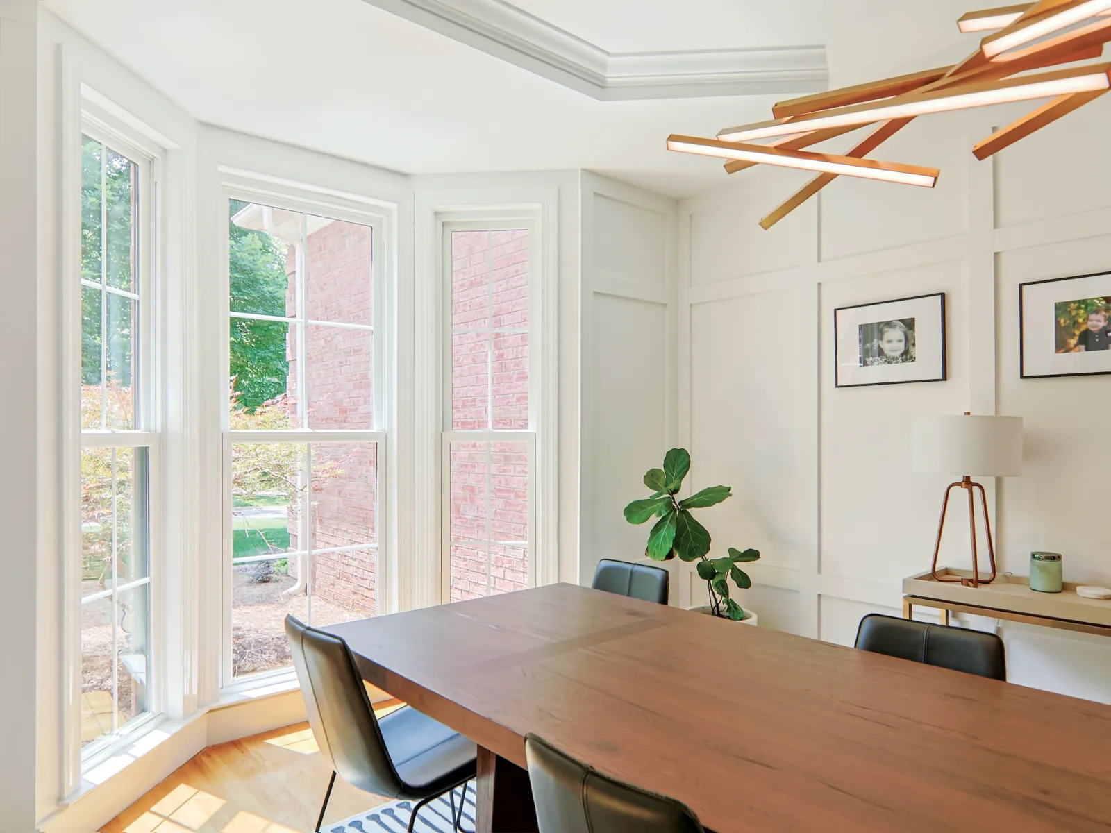 Bright dining room with large bay windows, wooden table, modern chairs, and contemporary chandelier.