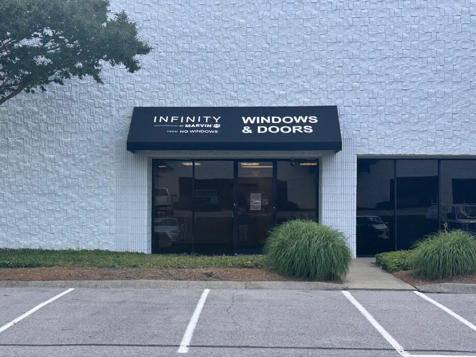 Storefront of Infinity by Marvin Windows & Doors with black awning and empty parking spaces outside.