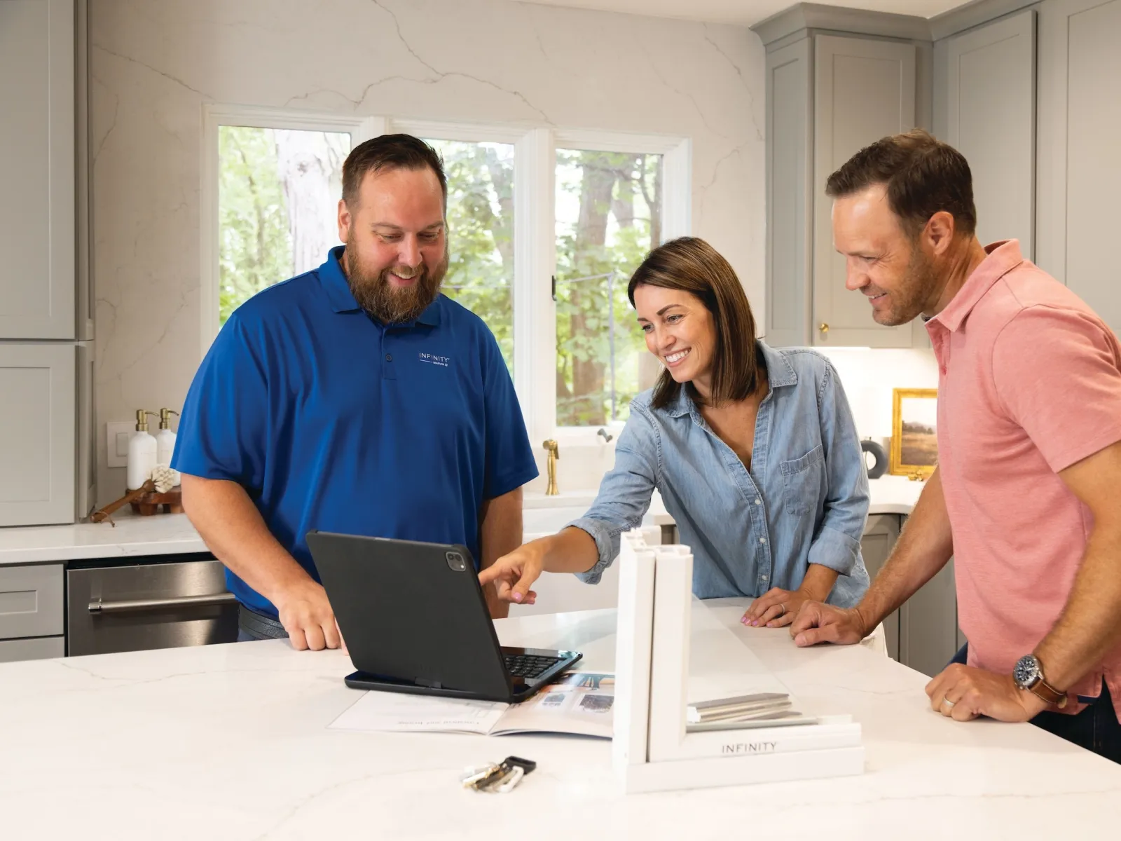 Three people smiling and discussing home renovation plans using a laptop in a modern kitchen.