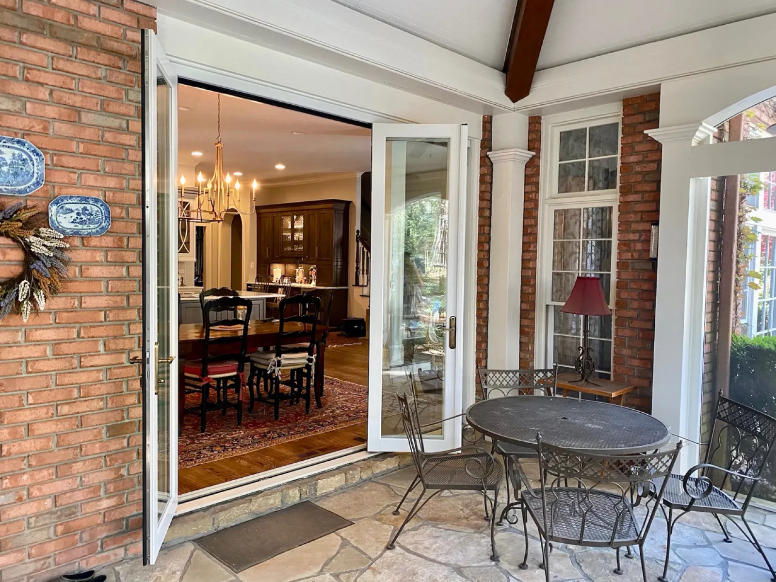 Patio with wrought iron table and chairs opens to indoor dining area with chandelier and wooden furniture