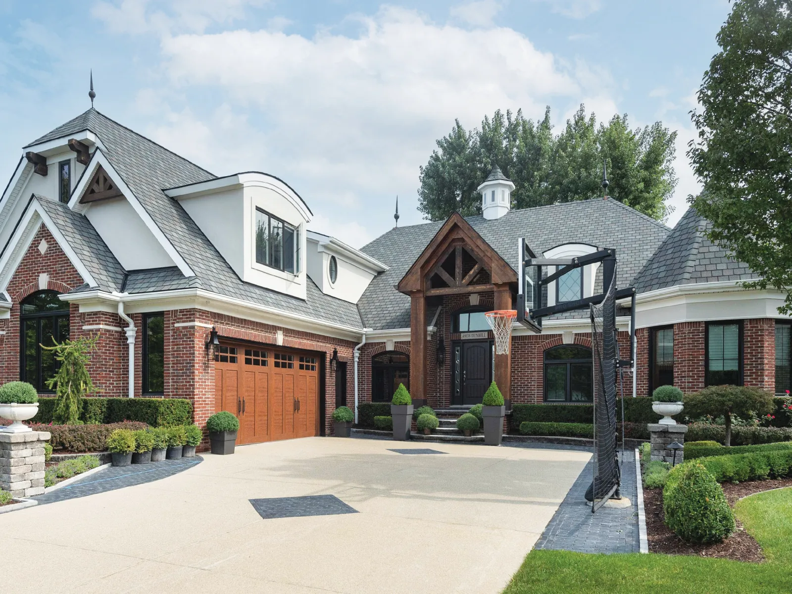 Elegant suburban home with brick facade, landscaped yard, and basketball hoop.