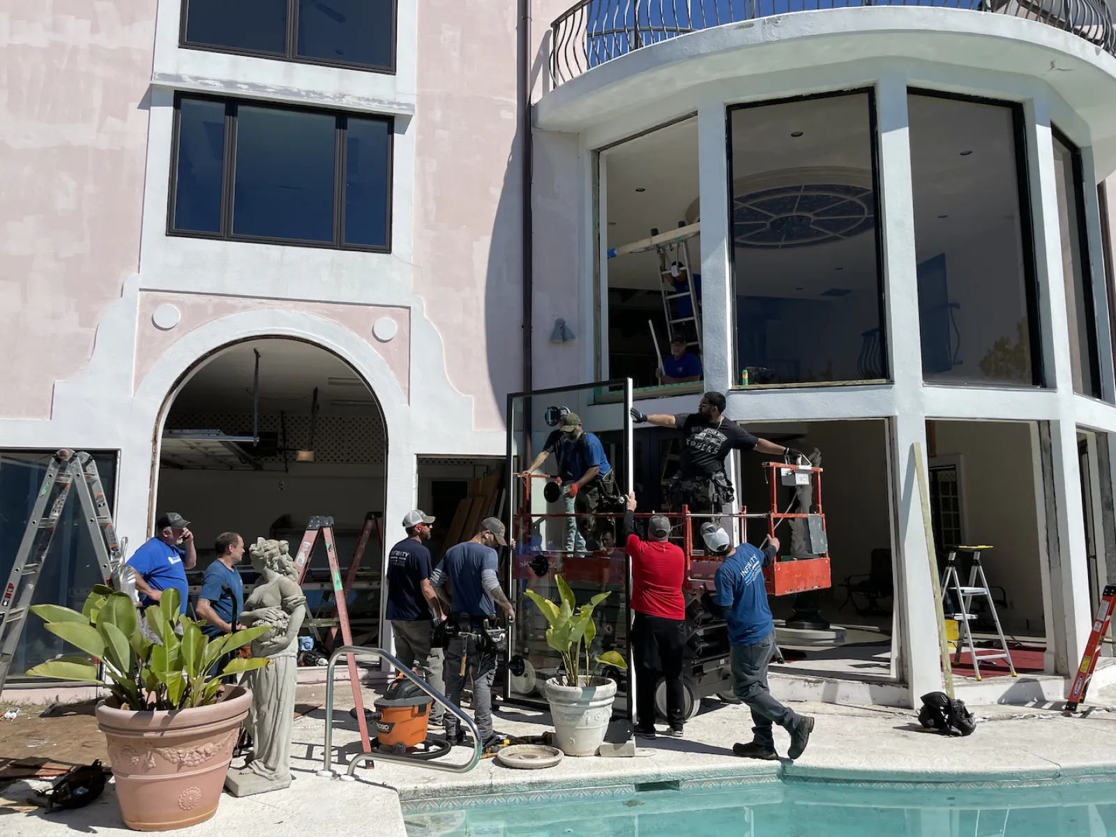Workers installing large glass windows in a residential building under construction near a swimming pool.