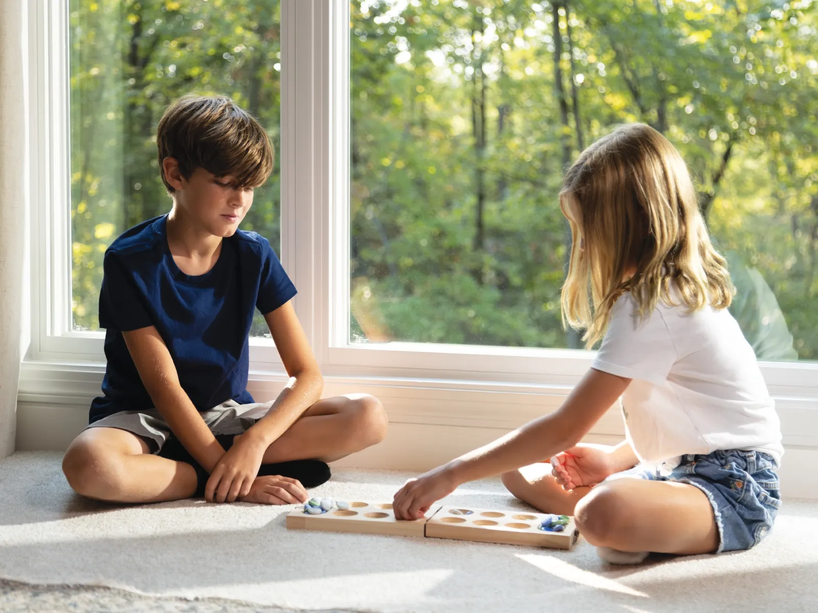 Two children playing a board game on a cozy carpet by a window with natural light.