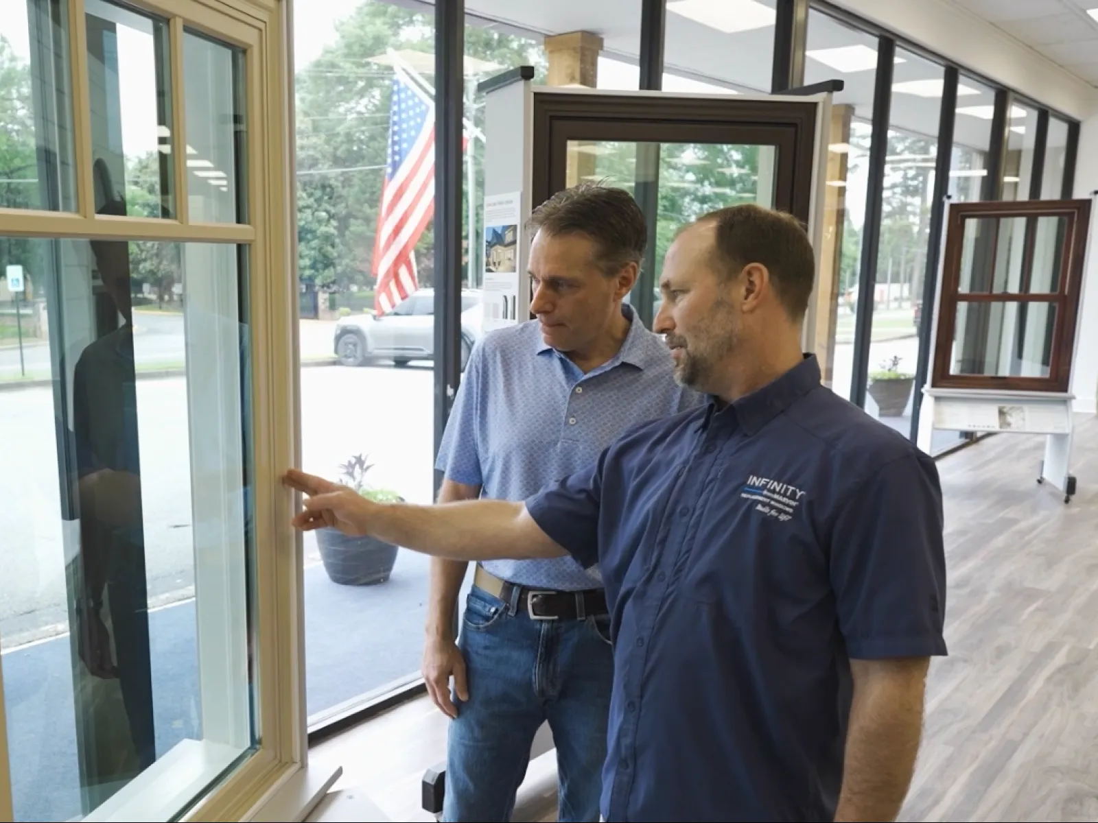 Two men discussing window features in a showroom with large glass windows and wood flooring.