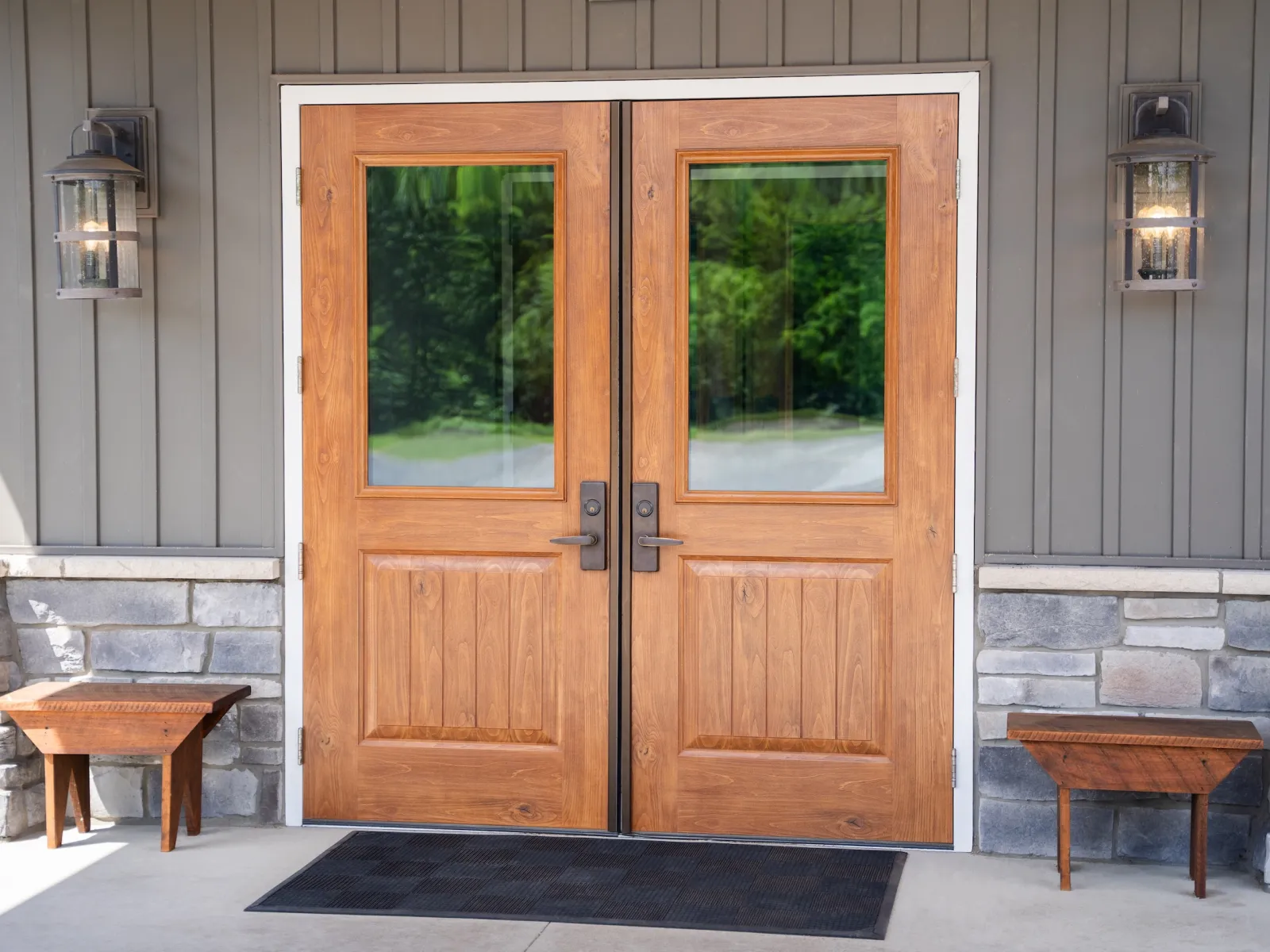 Double wooden front doors with glass panels, flanked by rustic benches and stone siding under lantern lights