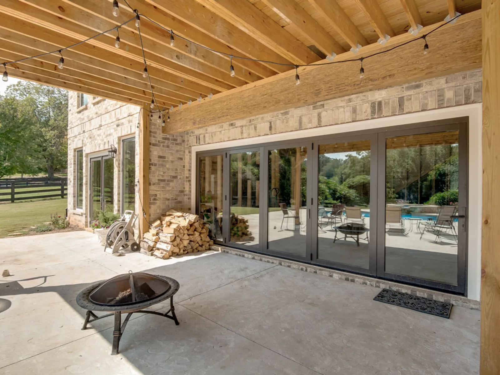 Covered patio area with fire pit, stacked firewood, and sliding glass doors reflecting outdoor pool and chairs.