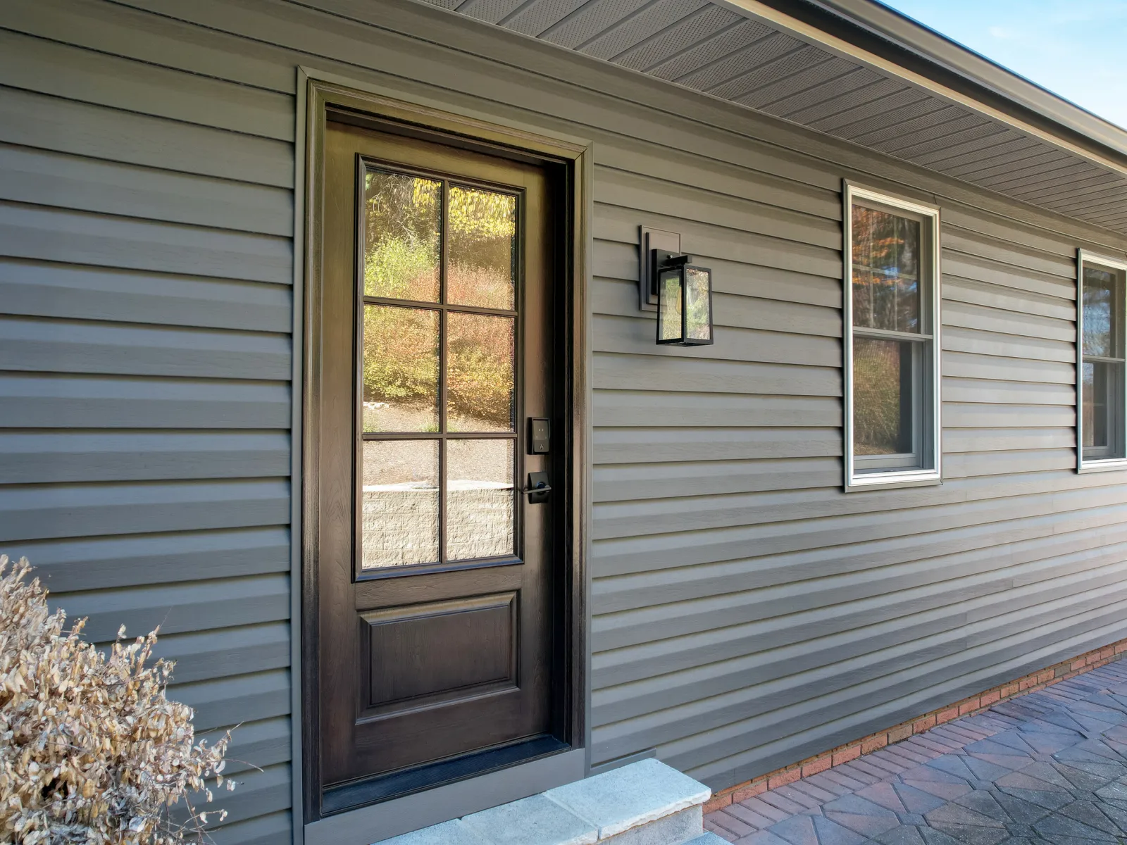 Modern gray vinyl siding with black framed glass door and two windows on house exterior under clear sky.