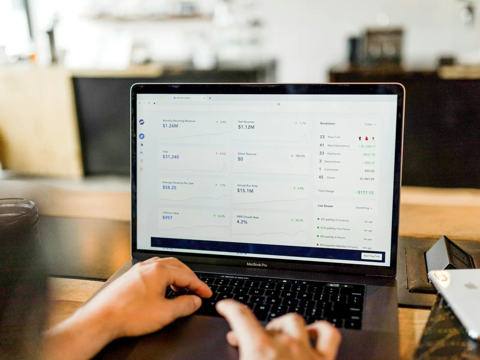Hands using MacBook Pro displaying financial dashboard with graphs and revenue data on screen.