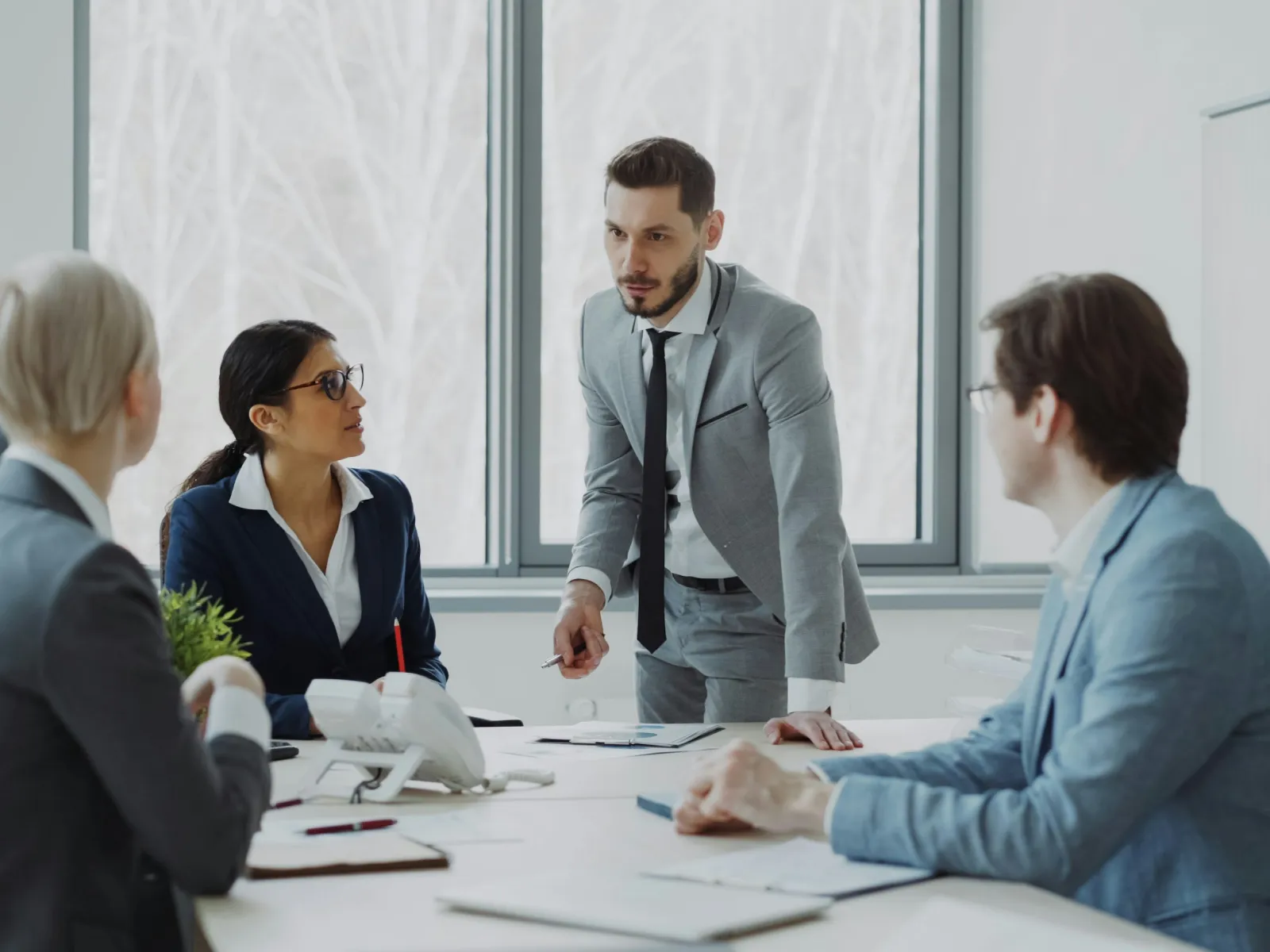 Four business professionals in a modern office having a serious discussion around a white table during a meeting.