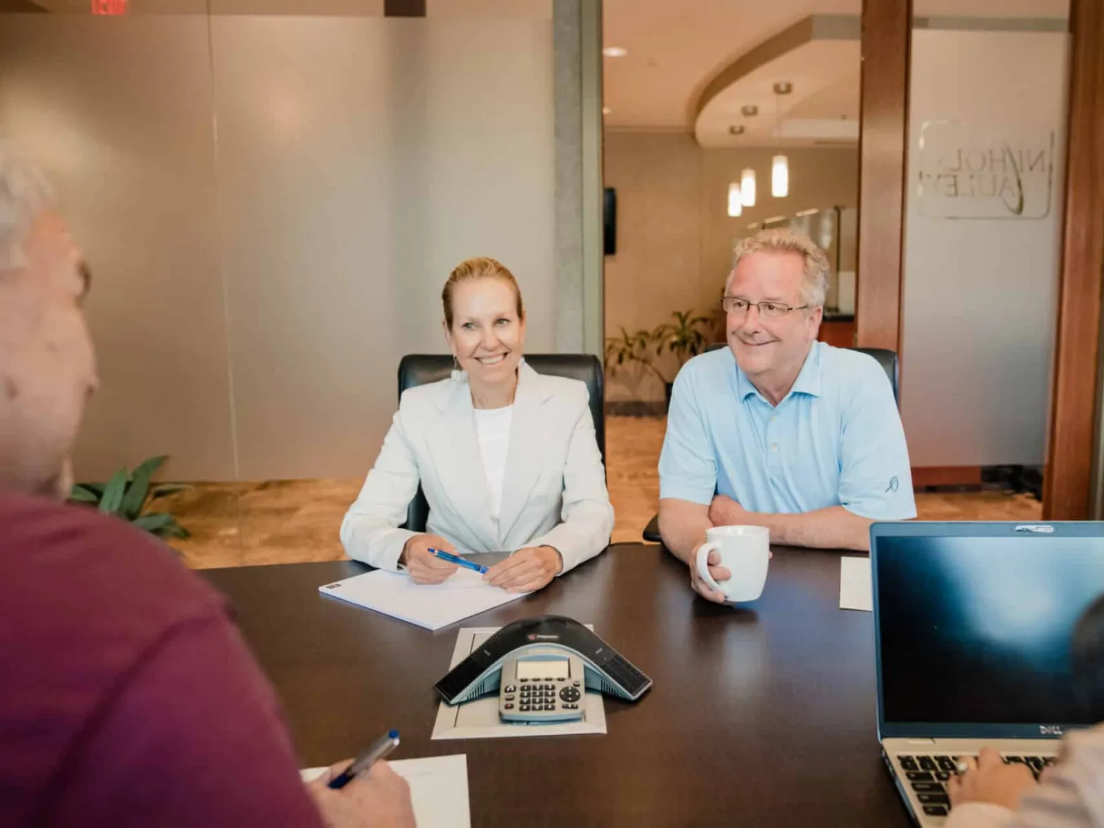 Business meeting with four professionals discussing around a conference table with laptop and speakerphone.