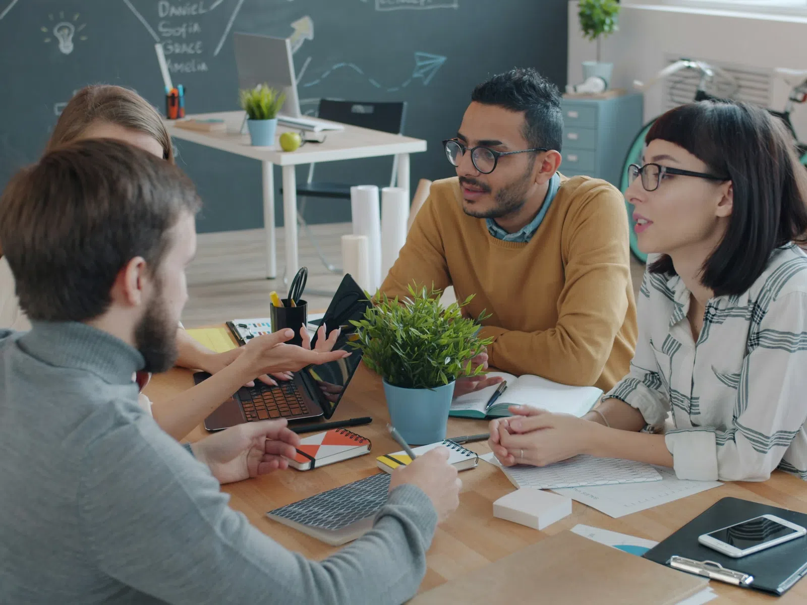 Young professionals collaborating on a project around a table with laptops and notes in a modern office.