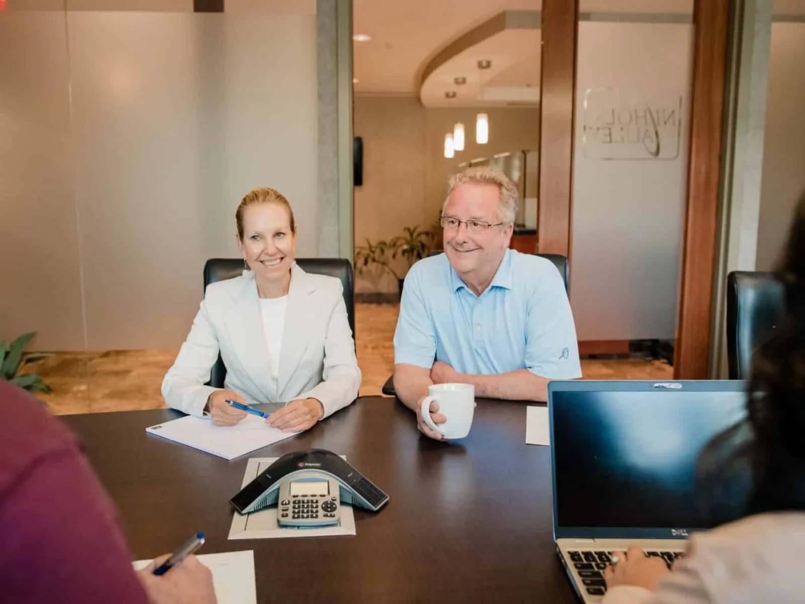 Two people smiling and talking during a business meeting with a laptop and conference phone on table