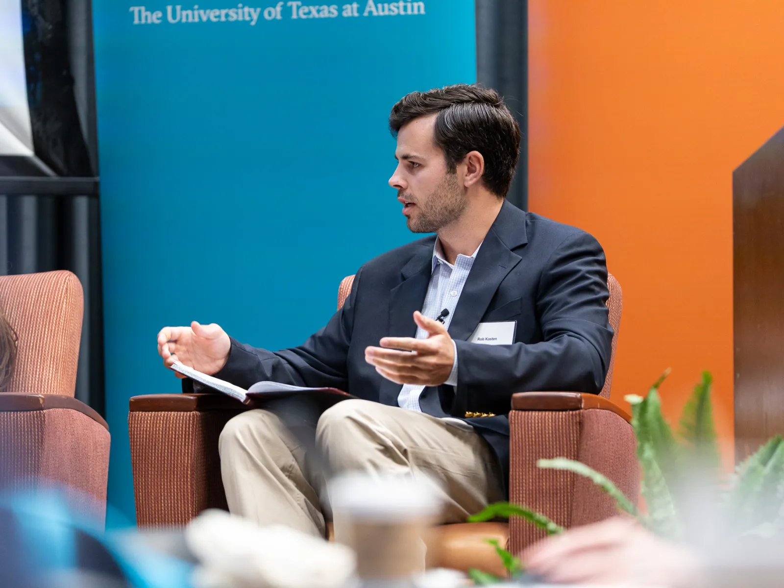 Man in blazer speaking and gesturing while seated during a discussion at University of Texas at Austin event